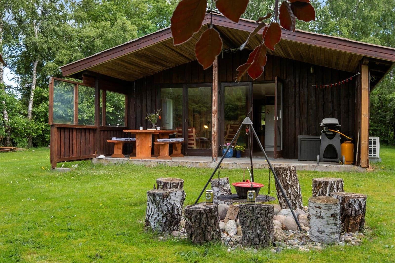 Holzhütte mit Grill, Tisch und Bänken im Garten. Rundum Grün und Bäume.