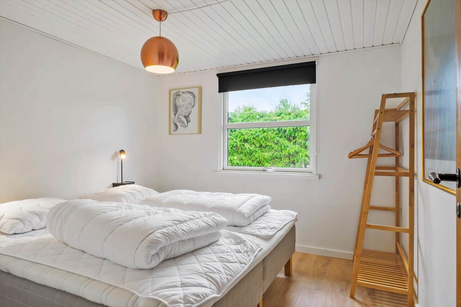 Schlafzimmer mit Doppelbett, Fenster mit Blick auf Bäume und Holzgarderobe.