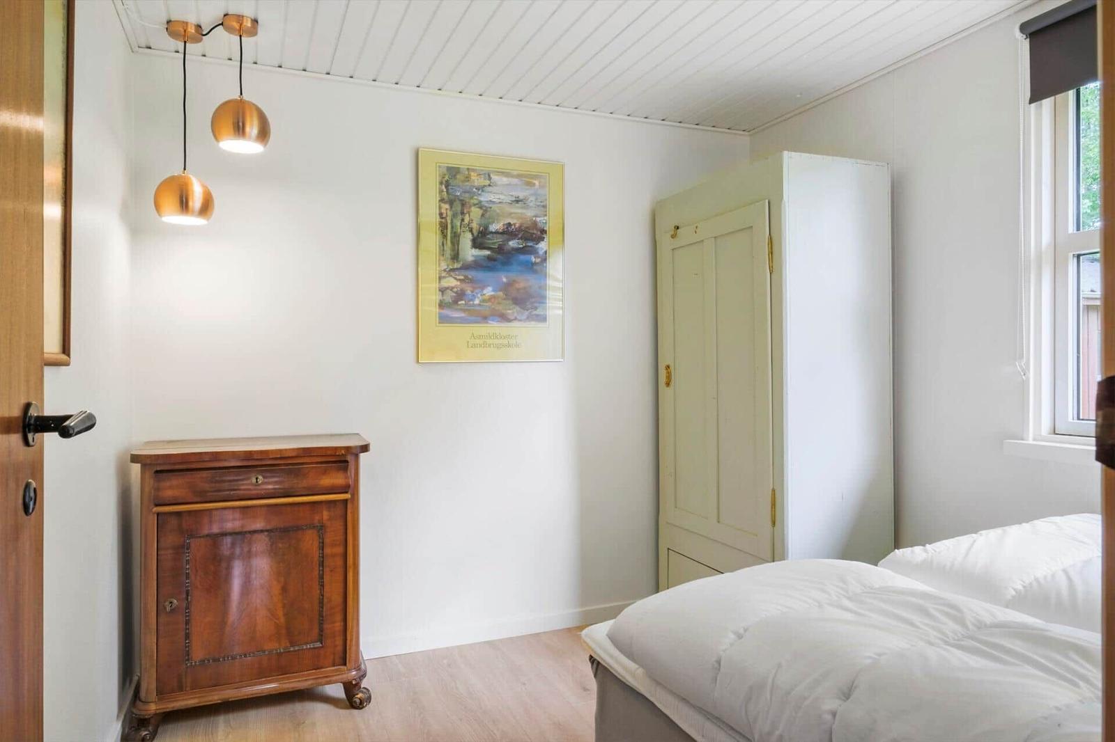 Schlafzimmer mit Bett, Kleiderschrank und Holzschrank. An der Wand hängt ein Bild.