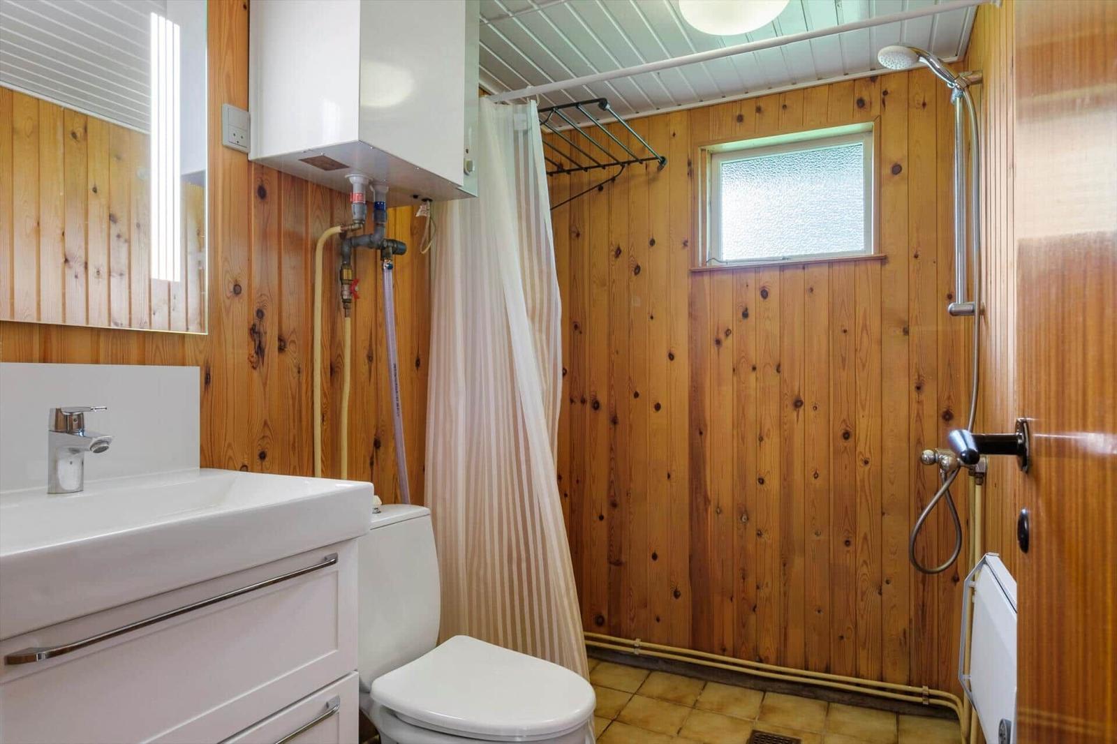 Badezimmer mit Holzwand, Dusche, Waschbecken und Toilette