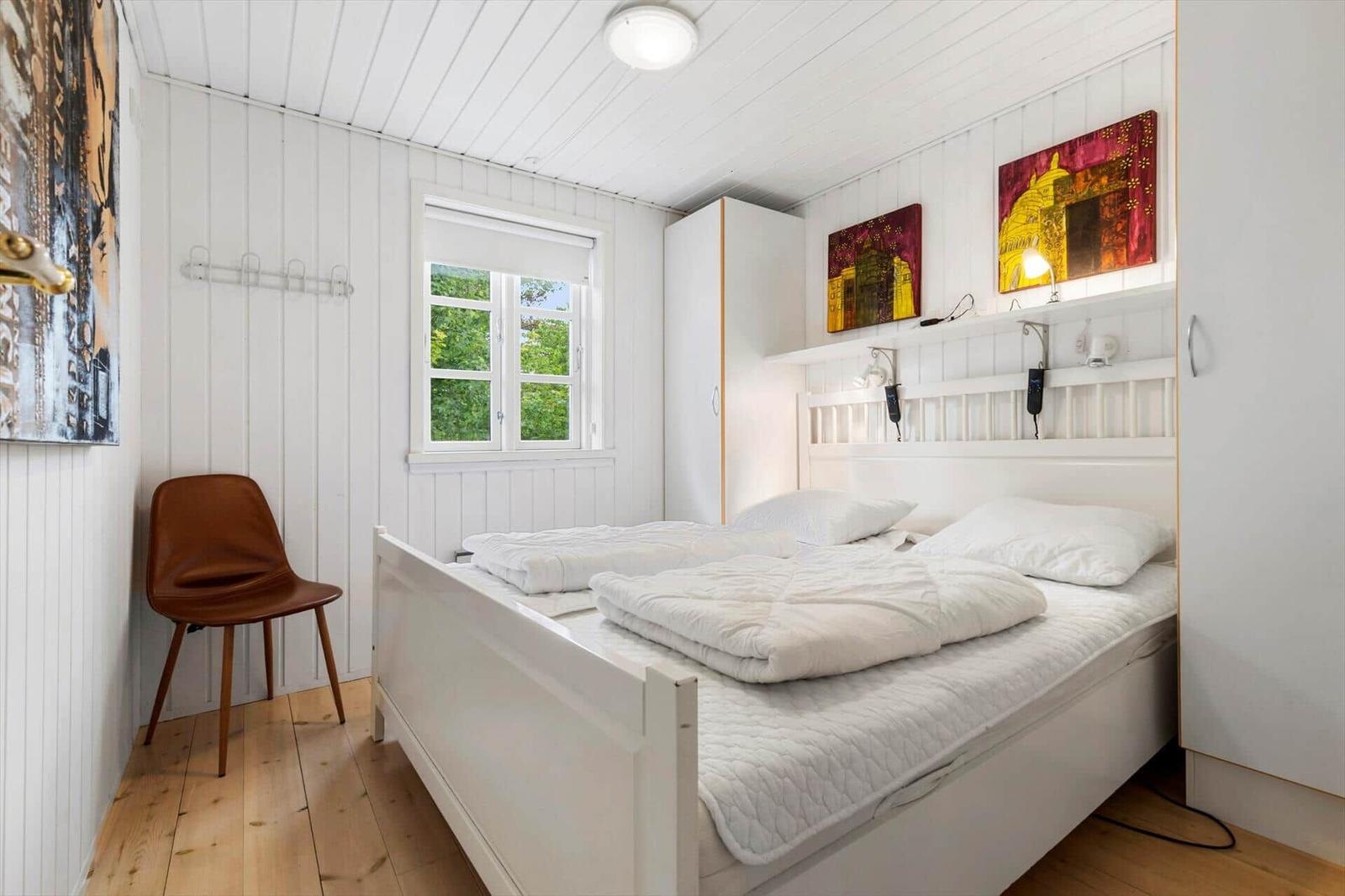 Ein Schlafzimmer mit weißem Bett, Holzboden und Fenster mit Blick auf Bäume.