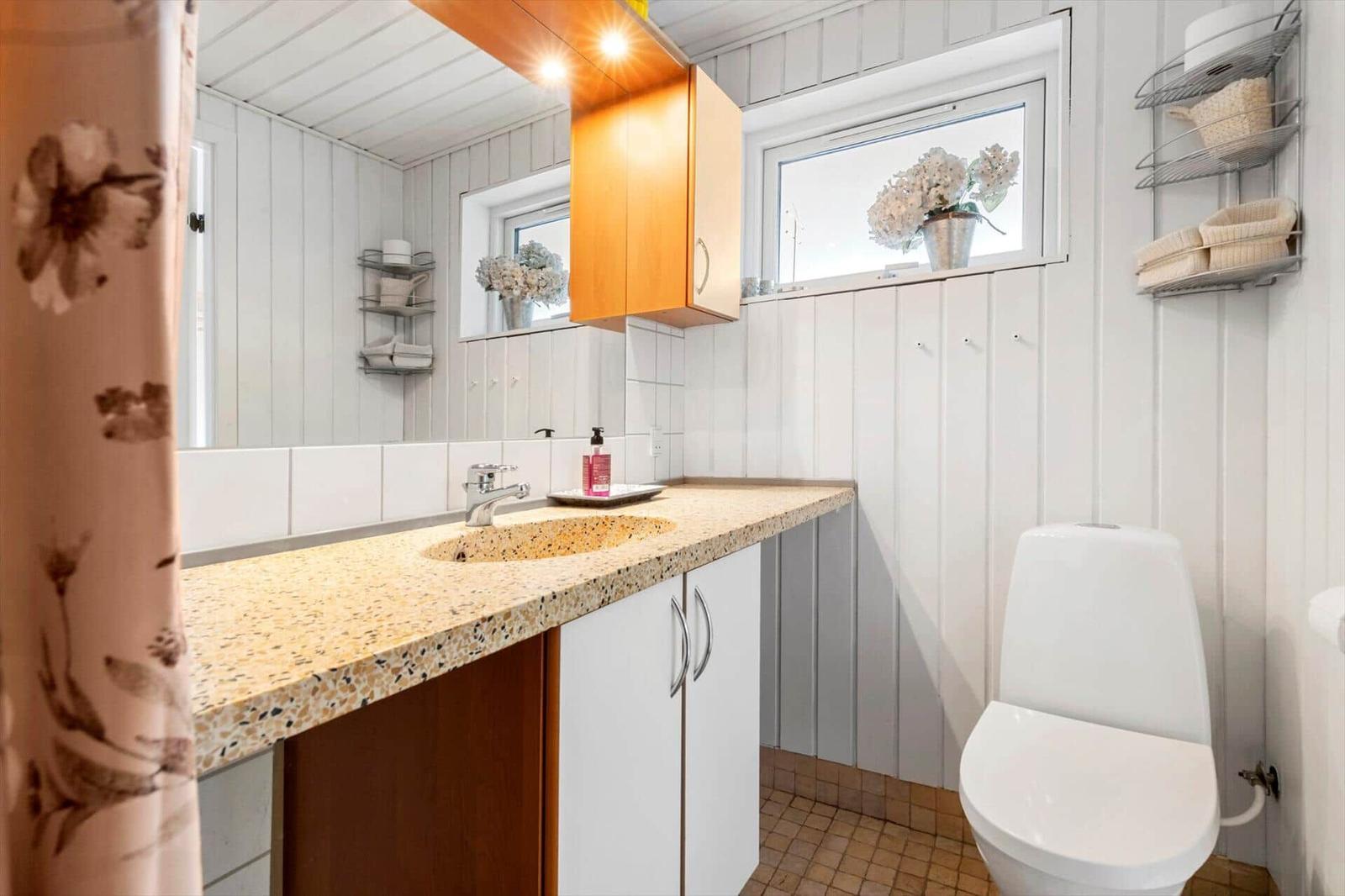 Badezimmer mit Waschbecken, Spiegel, Toilette und Fenster