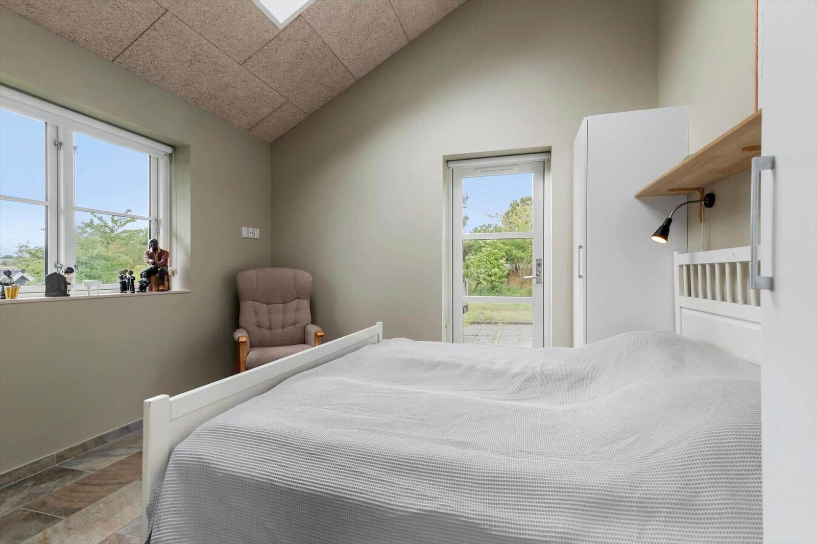 Schlafzimmer mit Bett, Sessel, Fenster und Tür. Decke mit Dachfenster.