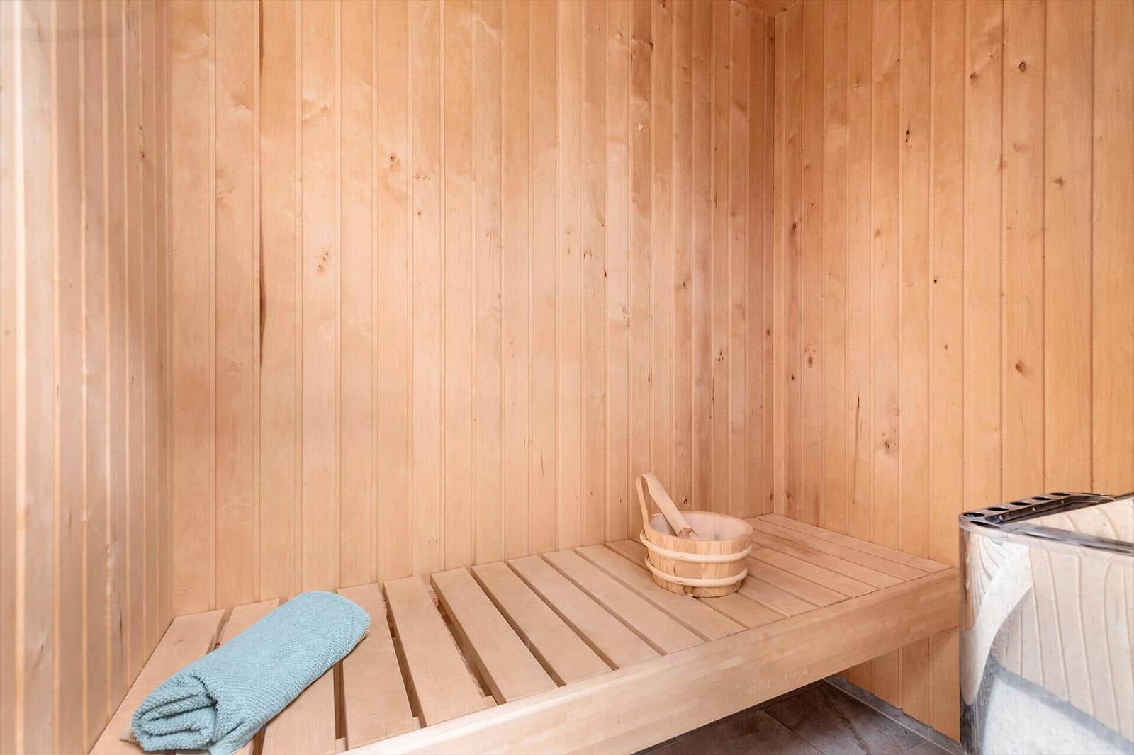 Sauna mit Holzwand, Bank, Holzschale und blauem Handtuch.