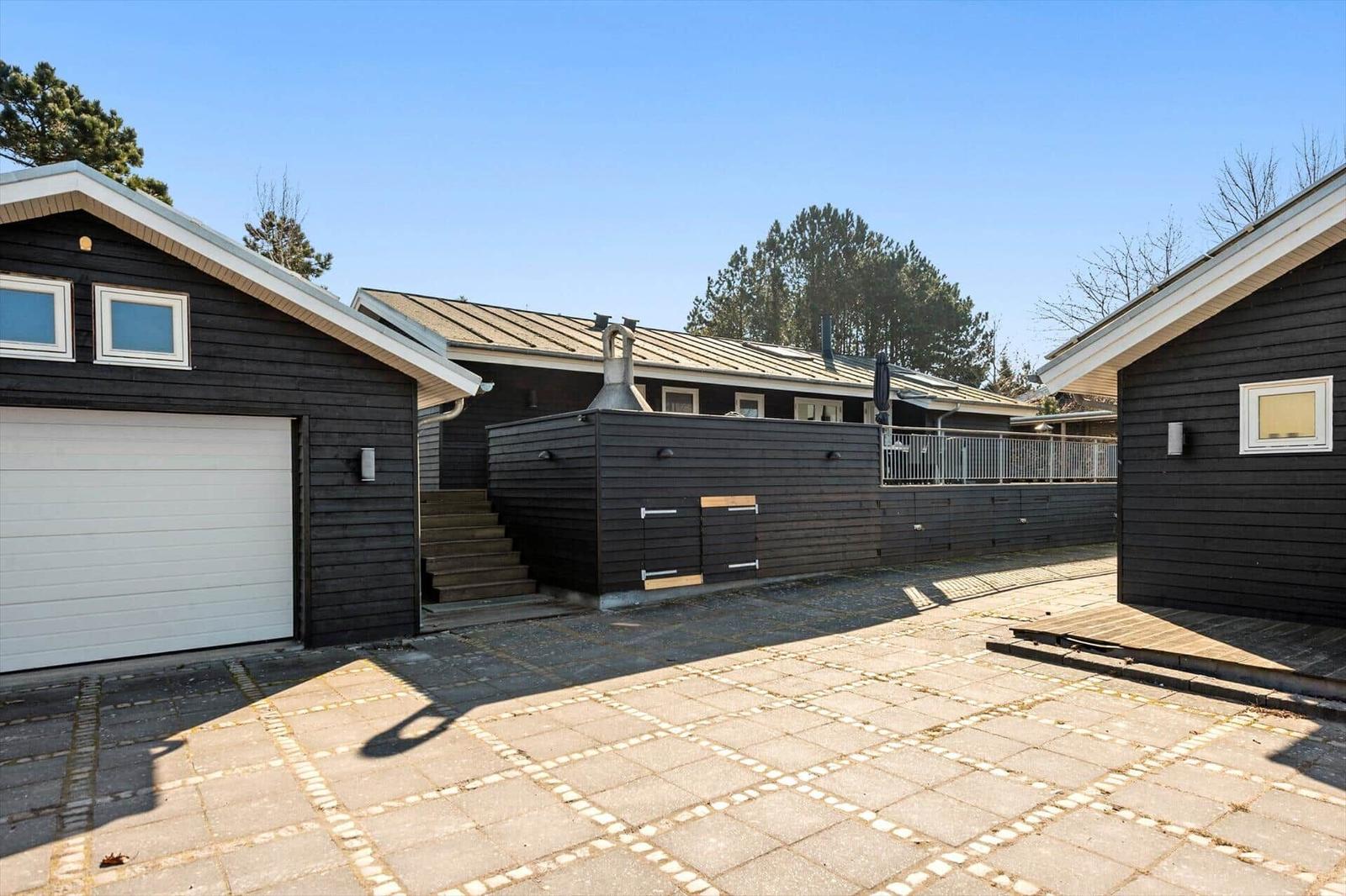 Schwarze Holzhäuser mit Garage und Terrasse unter blauem Himmel.