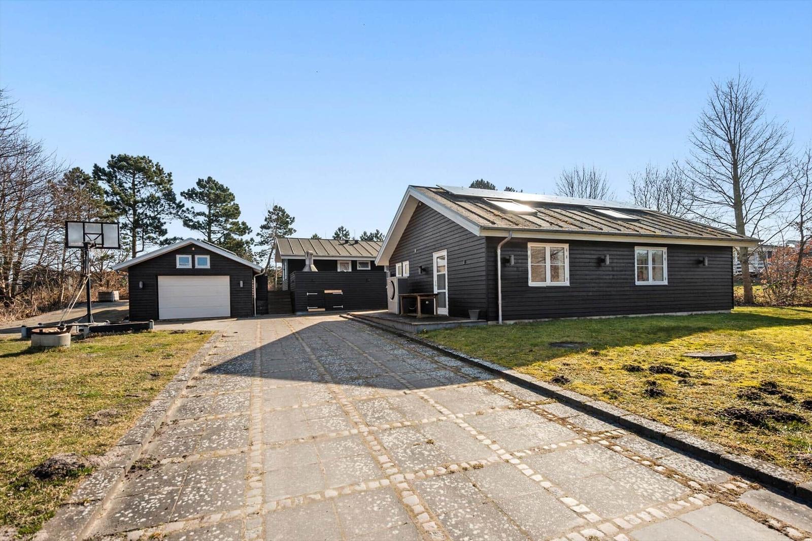 Schwarze Ferienhaus mit Garage und Basketballkorb im Freien.