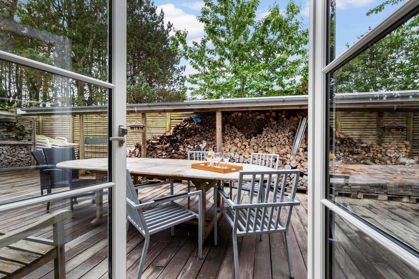 Terrasse mit Tisch und Stühlen, Holzstapel im Hintergrund, Blick in den Garten.