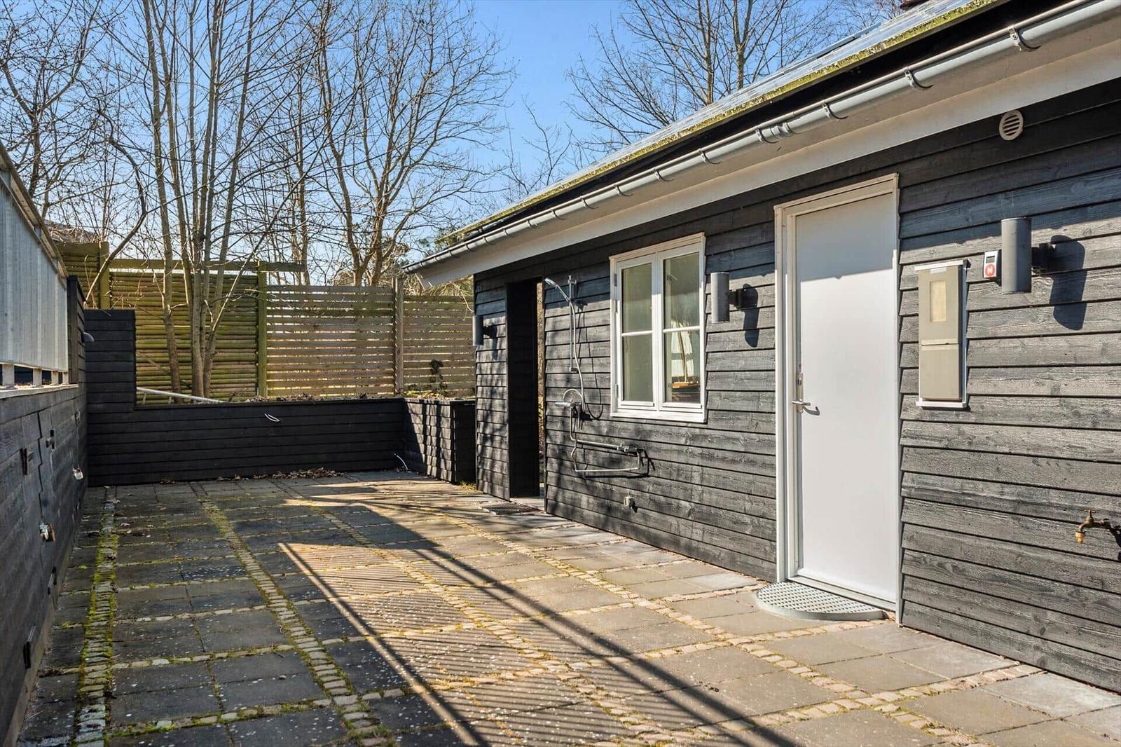 Hinterhof mit Steinplatten, weiße Tür und Fenster, Dusche im Freien.