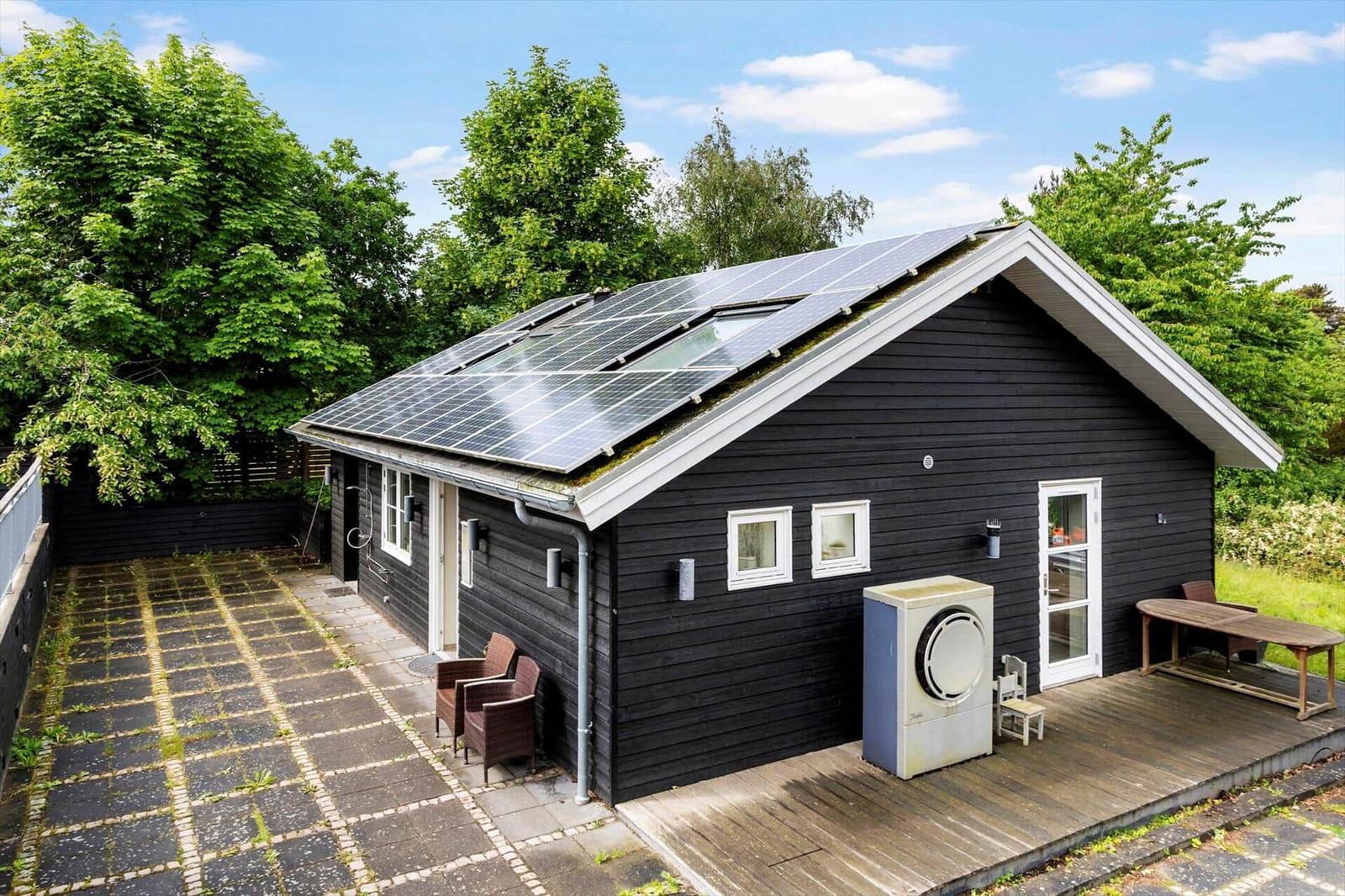 Schwarzes Haus mit Solaranlage, Terrasse und Garten. Außenbereich mit Tisch und Stühlen.