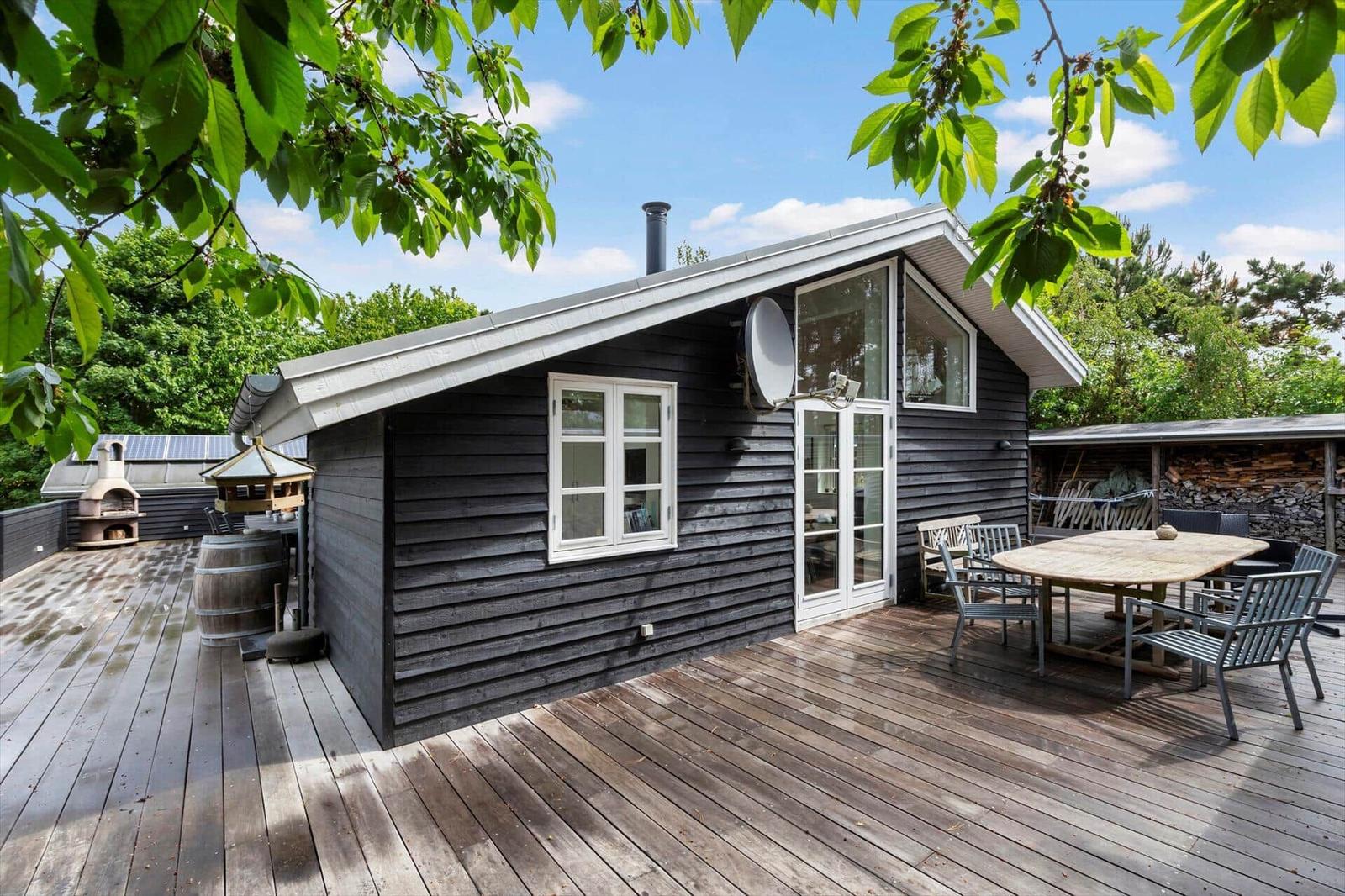 Holzhaus mit Terrasse, Tisch, Stühlen und Grillplatz im Freien.