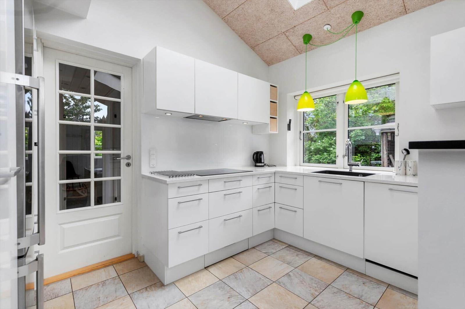 Küche mit weißen Schränken, Fenster und grünen Hängelampen.