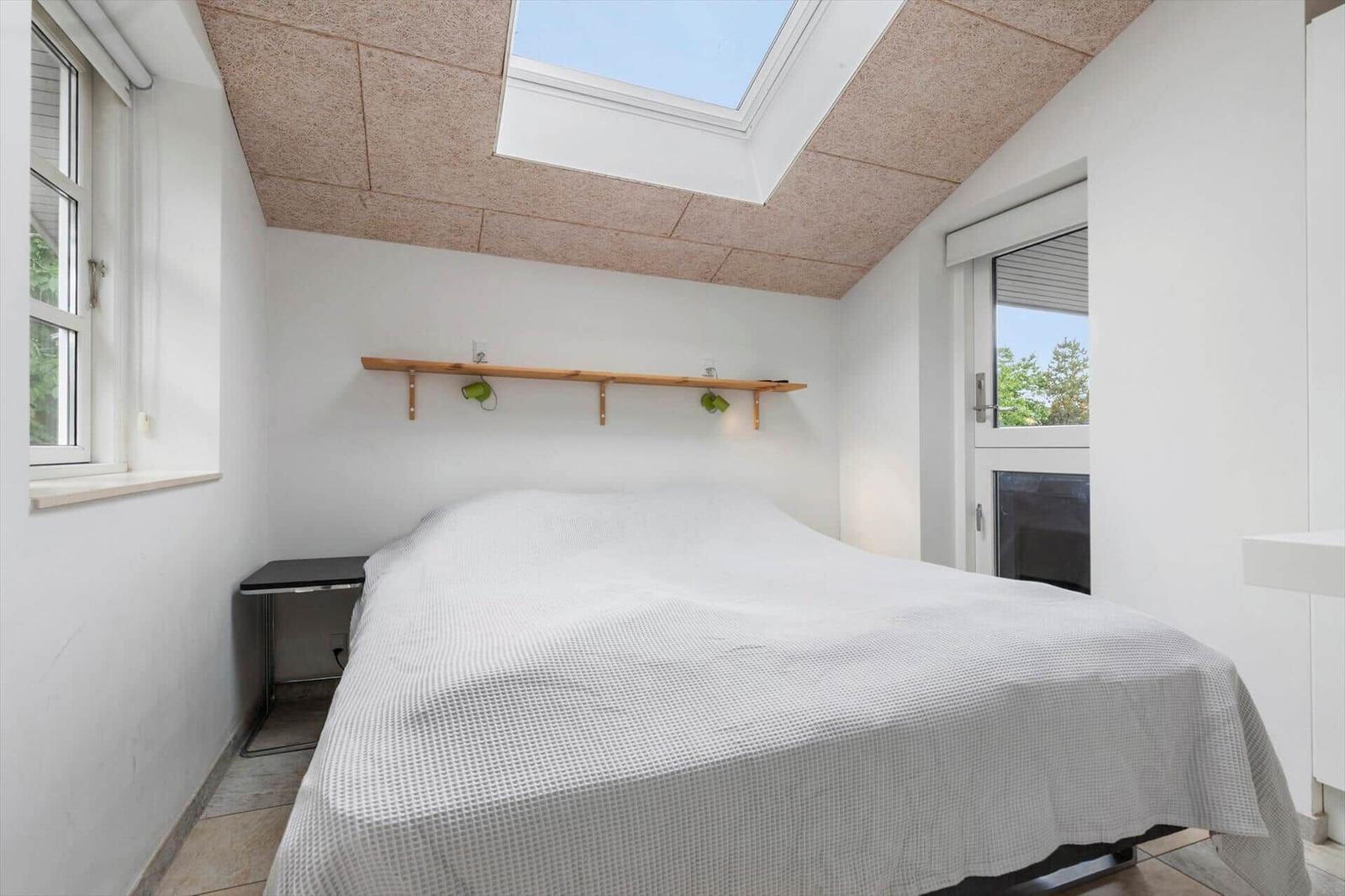 Schlafzimmer mit Dachfenster, Bett und Schrank. Fenster und Tür zur Außenseite.