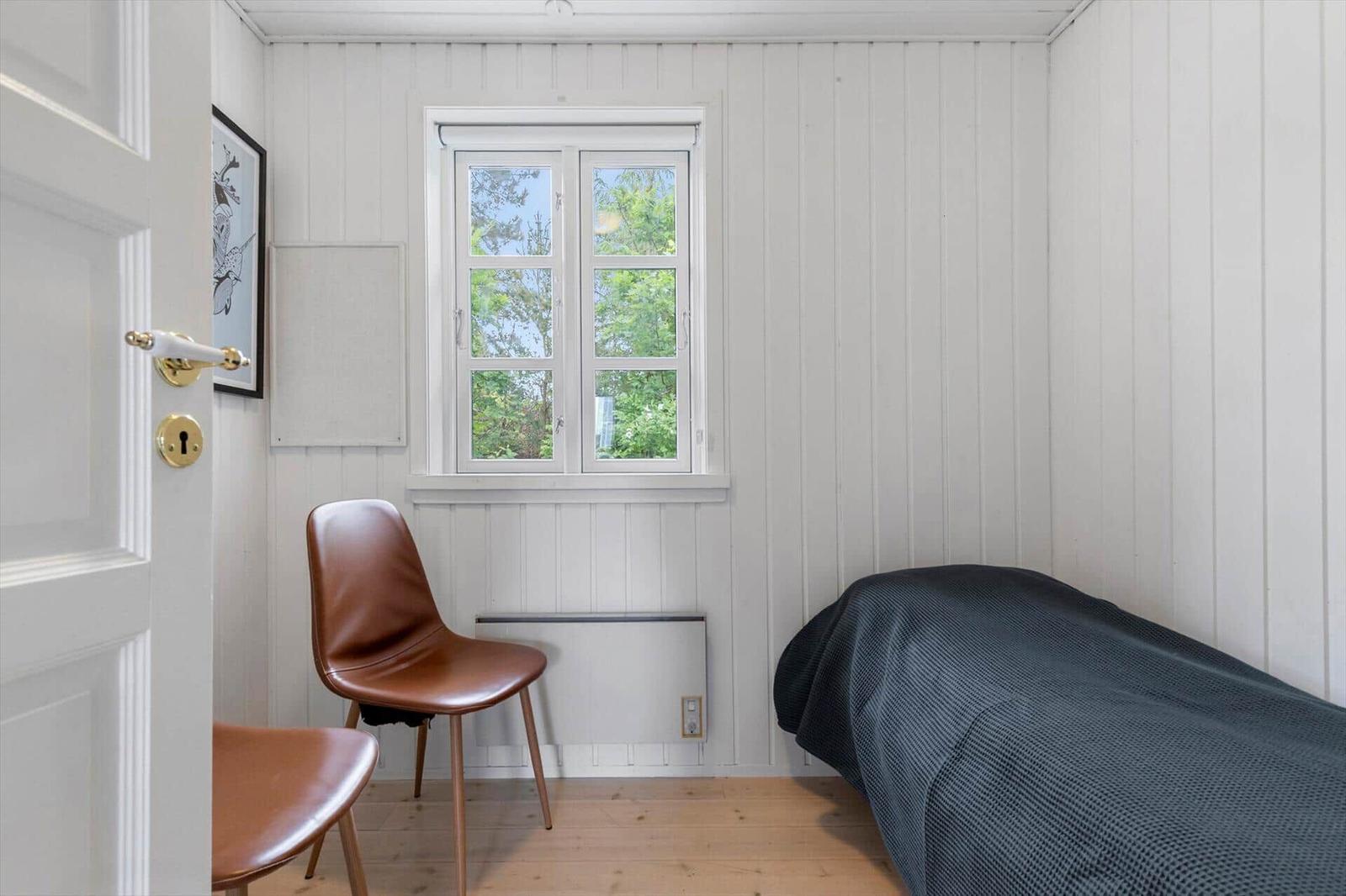 Ein Raum mit weiß verputzten Wänden, einem Fenster, einem Stuhl und einem Bett.