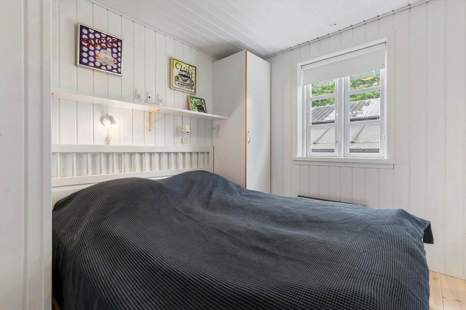 Schlafzimmer mit Bett, Wandregal und Fenster. Wände sind weiß verputzt.