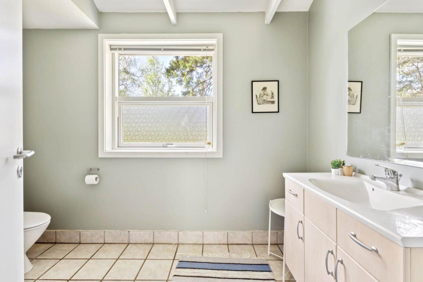 Badezimmer mit Waschbecken, Toilette und Fenster mit Blick auf Bäume.