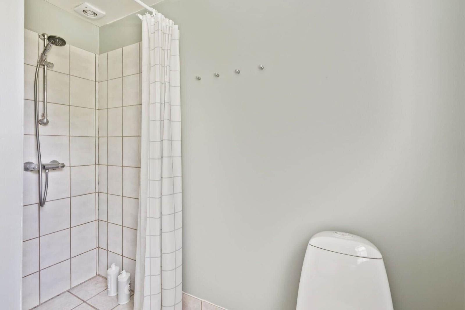 Dusche mit Duschbrause, Toilette und weiße Wand mit Haken.