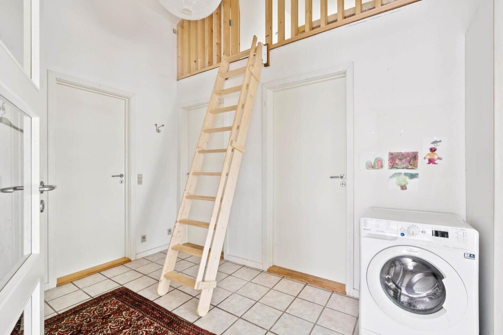 Haus mit Holztreppe zur oberen Etage und Waschmaschine in einem Raum mit Fliesenboden.
