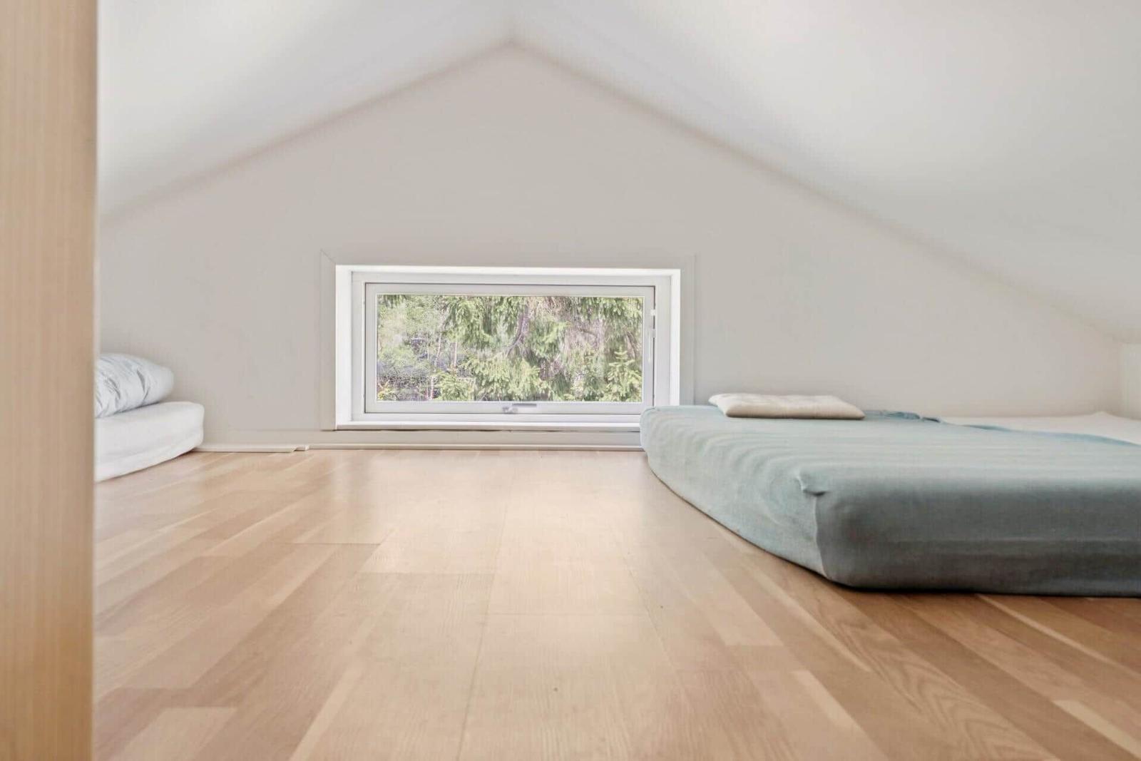 Schlafzimmer mit Holzboden, Fenster und Matratze.