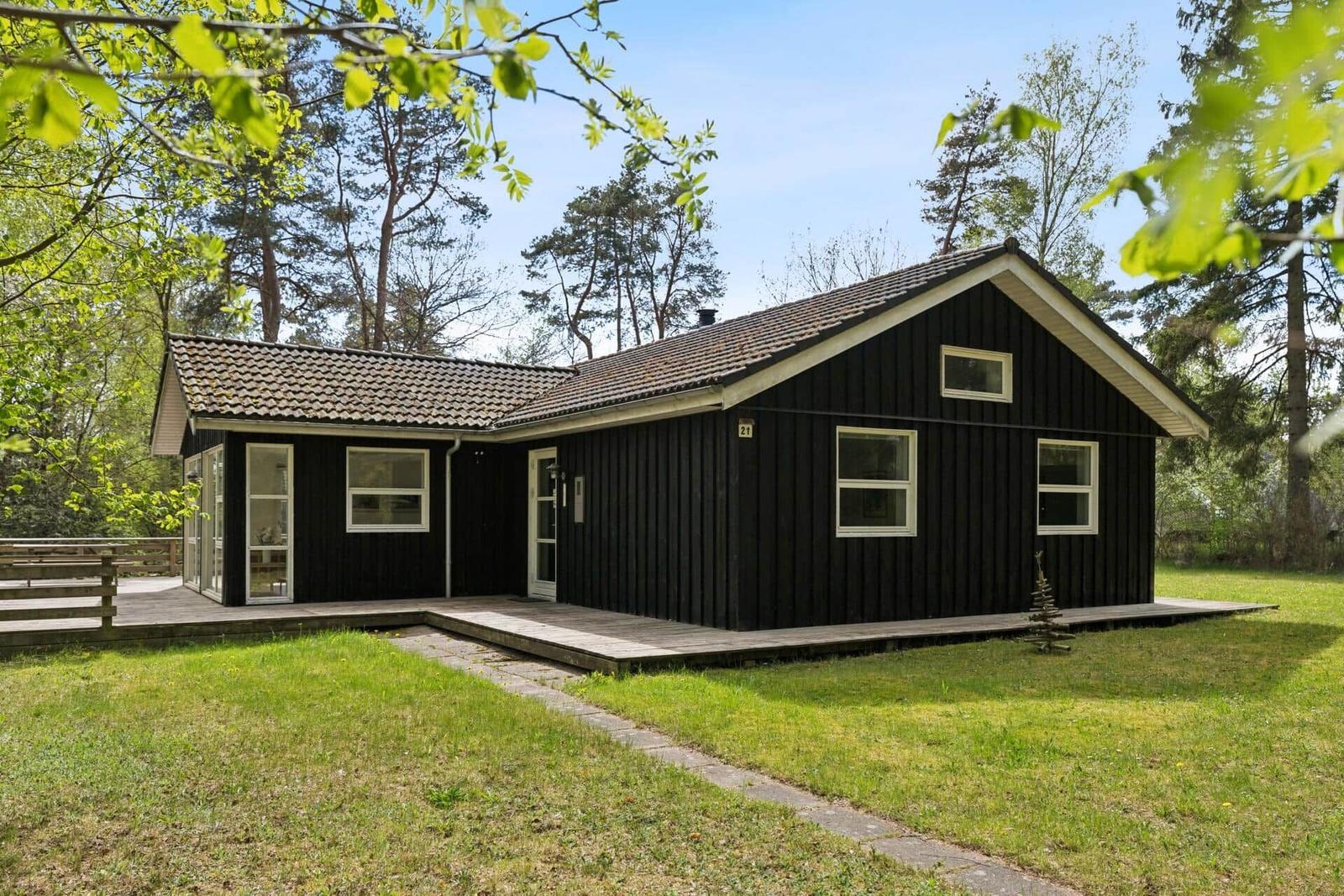 Schwarzes Holzhaus mit Terrasse und Garten im Wald. Fenster und Tür sind weiß.