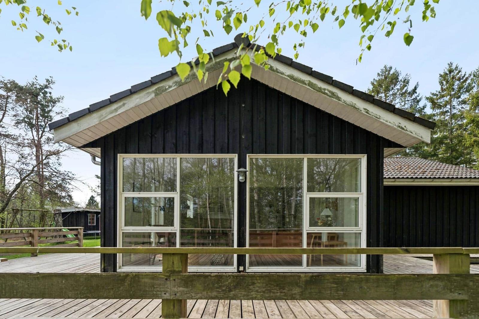 Holzhaus mit großer Fensterfront und Holzterrasse im Wald.