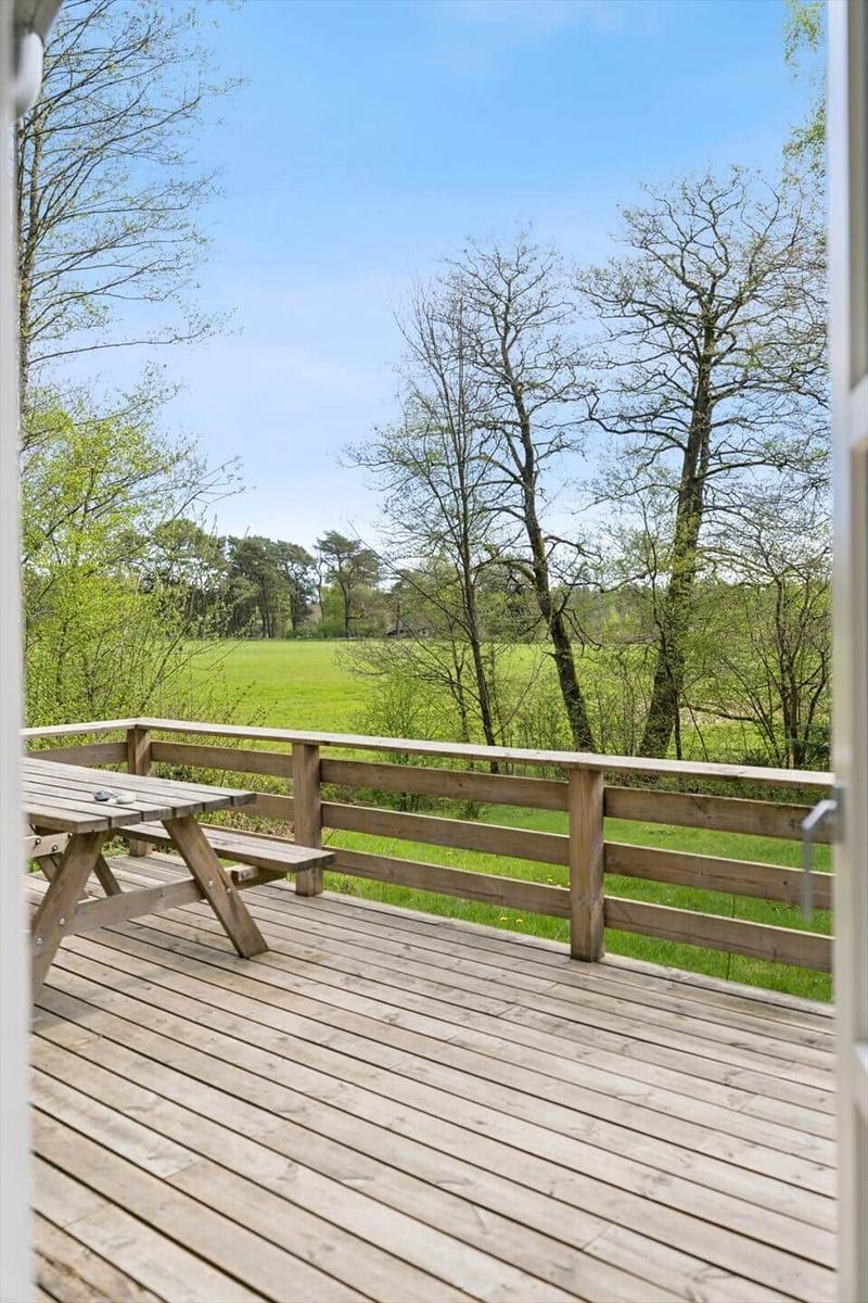 Holzterrasse mit Picknicktisch und Blick auf grünes Feld und Bäume.