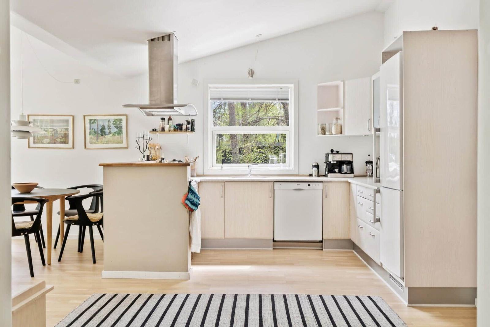 Küche mit Essbereich, Fenster, Spüle, Kühlschrank und Dunstabzug.