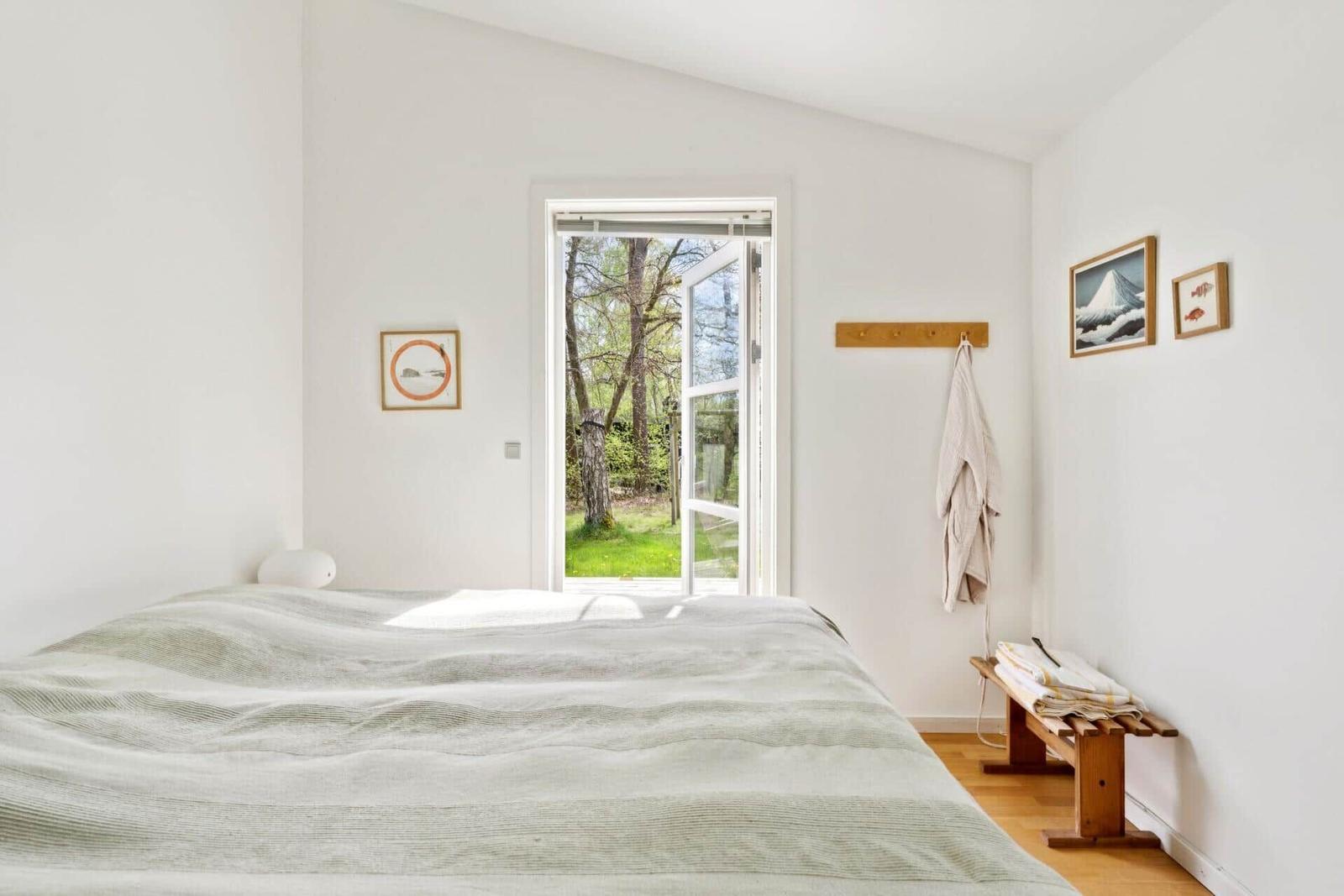 Schlafzimmer mit Bett, Fenster zur grünen Außenseite und Holzbank mit Handtüchern.