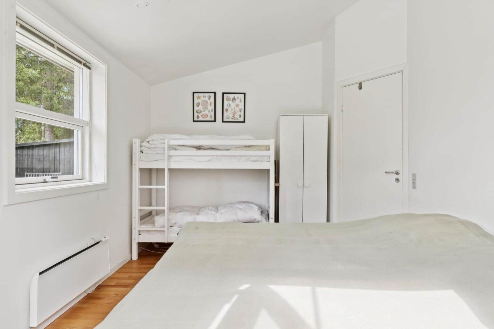 Zimmer mit Doppelbett, Etagenbett und Fenster mit Blick auf Grün.