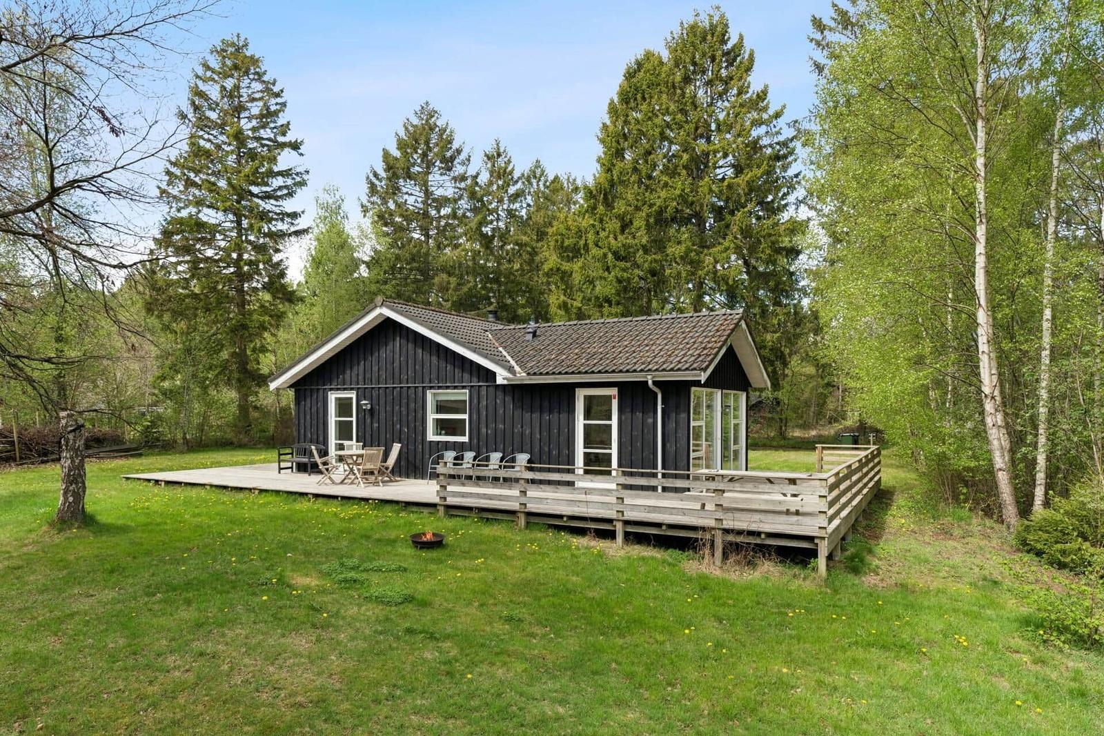 Schwarzes Holzhaus mit Terrasse, Grill und Garten in Waldnähe.