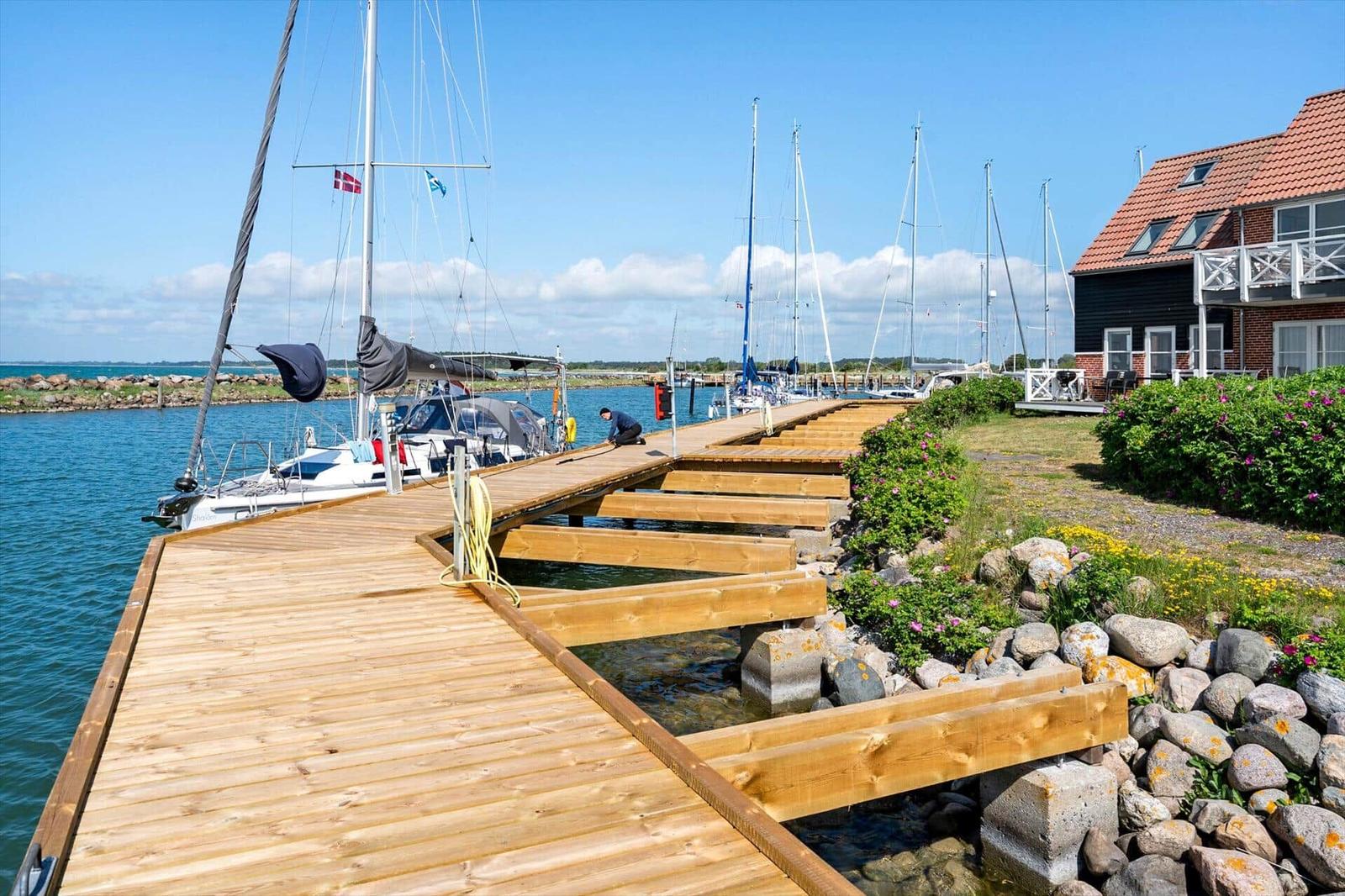 Holzsteg führt zum Wasser mit Booten und Haus im Hintergrund.