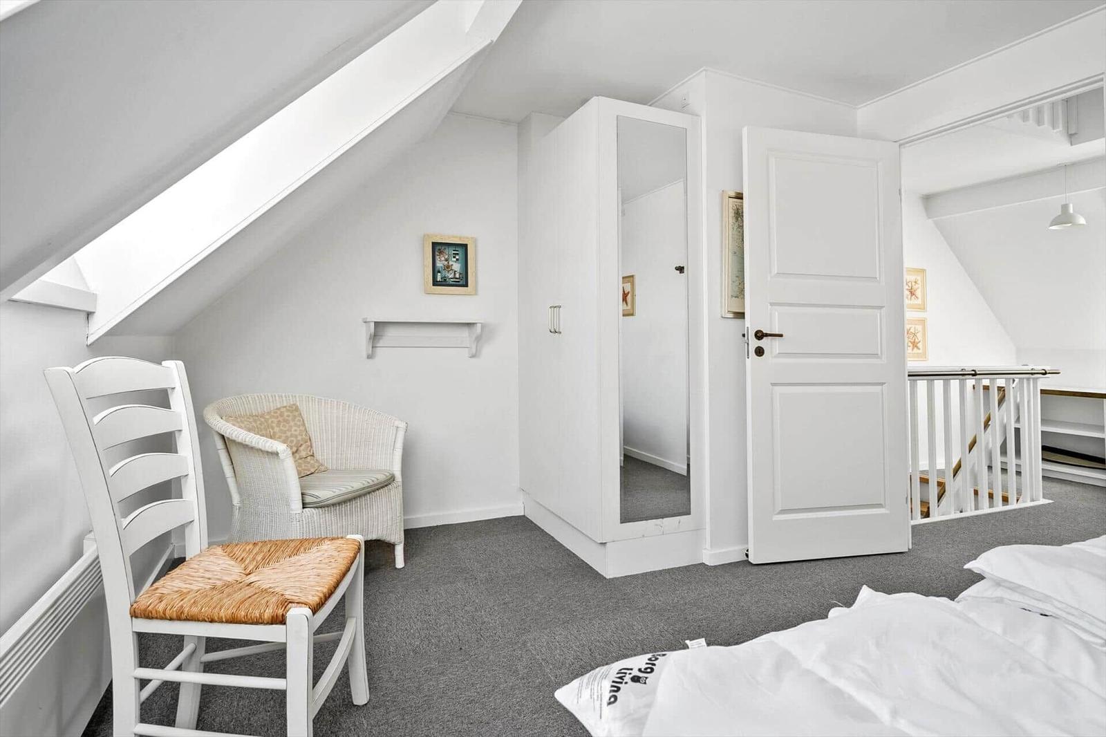 Schlafzimmer mit Dachschrägen, weißer Tür, Kleiderschrank und Stuhl.