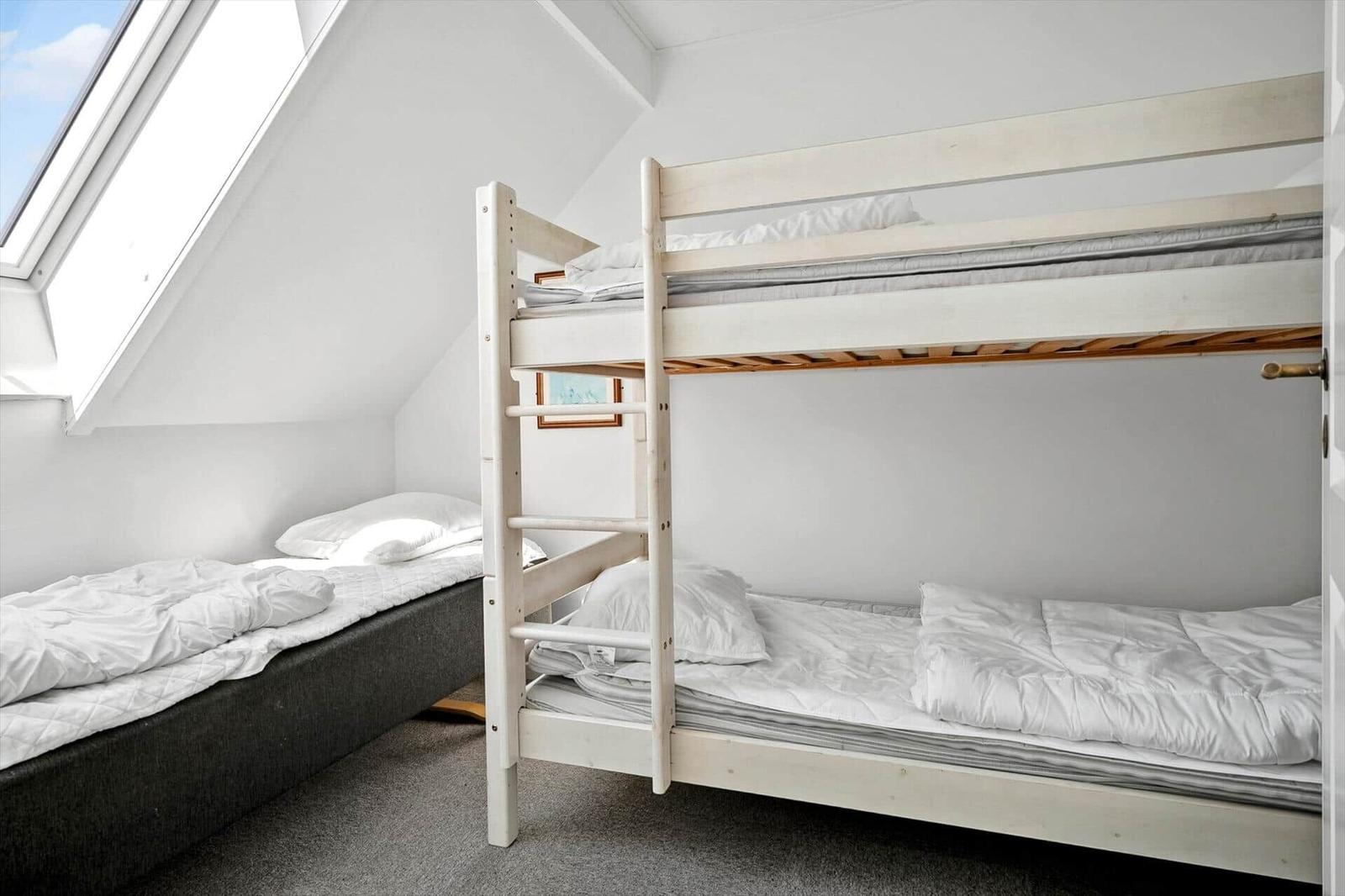 Zimmer mit Doppelstockbett und Einzelbett unter Dachschräge mit Dachfenster.