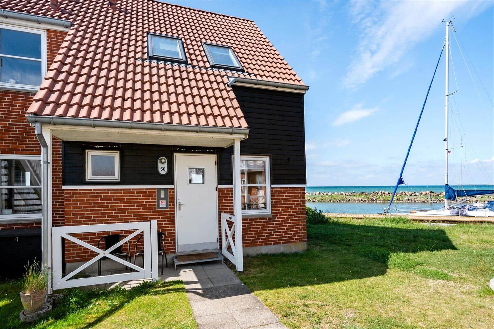 Haus mit rotem Dach, weiße Tür und Garten. Boot liegt am Wasser.