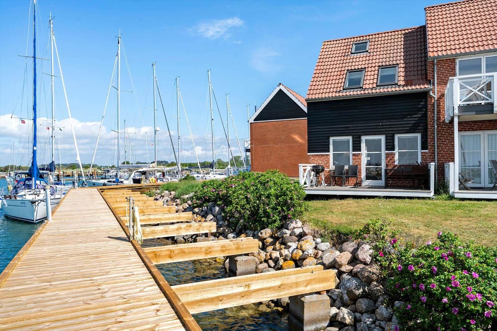 Haus mit Terrasse neben Steg und Booten im Hafen.