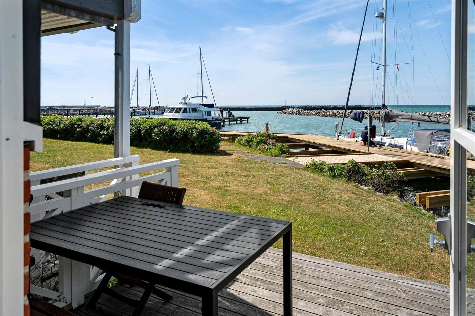 Terrasse mit Tisch und Stuhl, Blick auf Hafen mit Booten und Grünflächen.