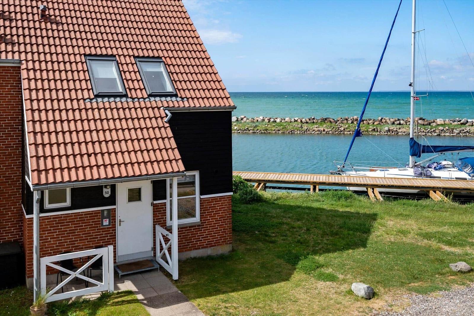 Haus mit rotem Dach und Bootssteg am Wasser.