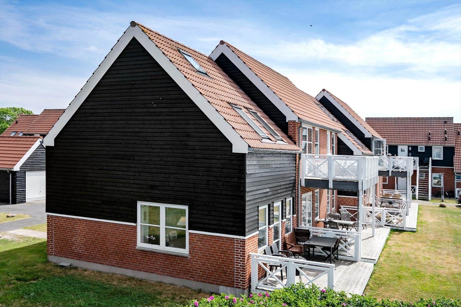 Holzhaus mit Terrasse und Garten. Roter Ziegeldach. Weiße Fenster und Geländer.