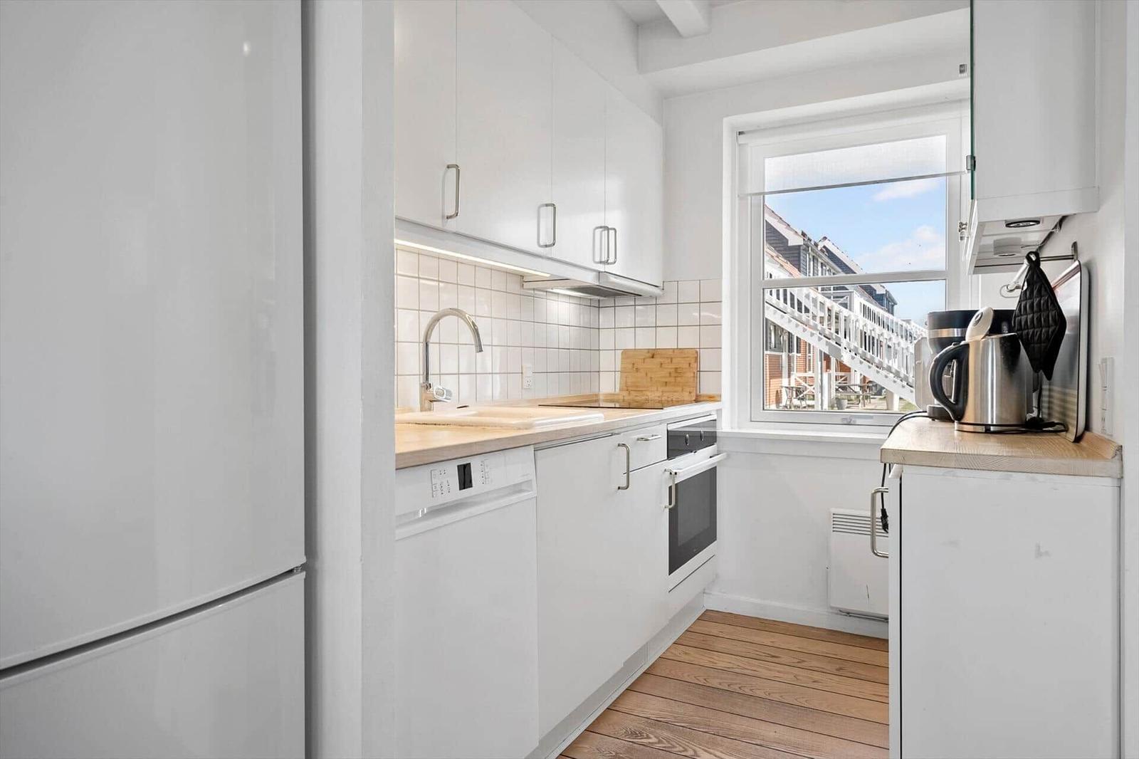 Küche mit weißen Schränken, Holzoberfläche und Fensterblick auf Außentreppe.