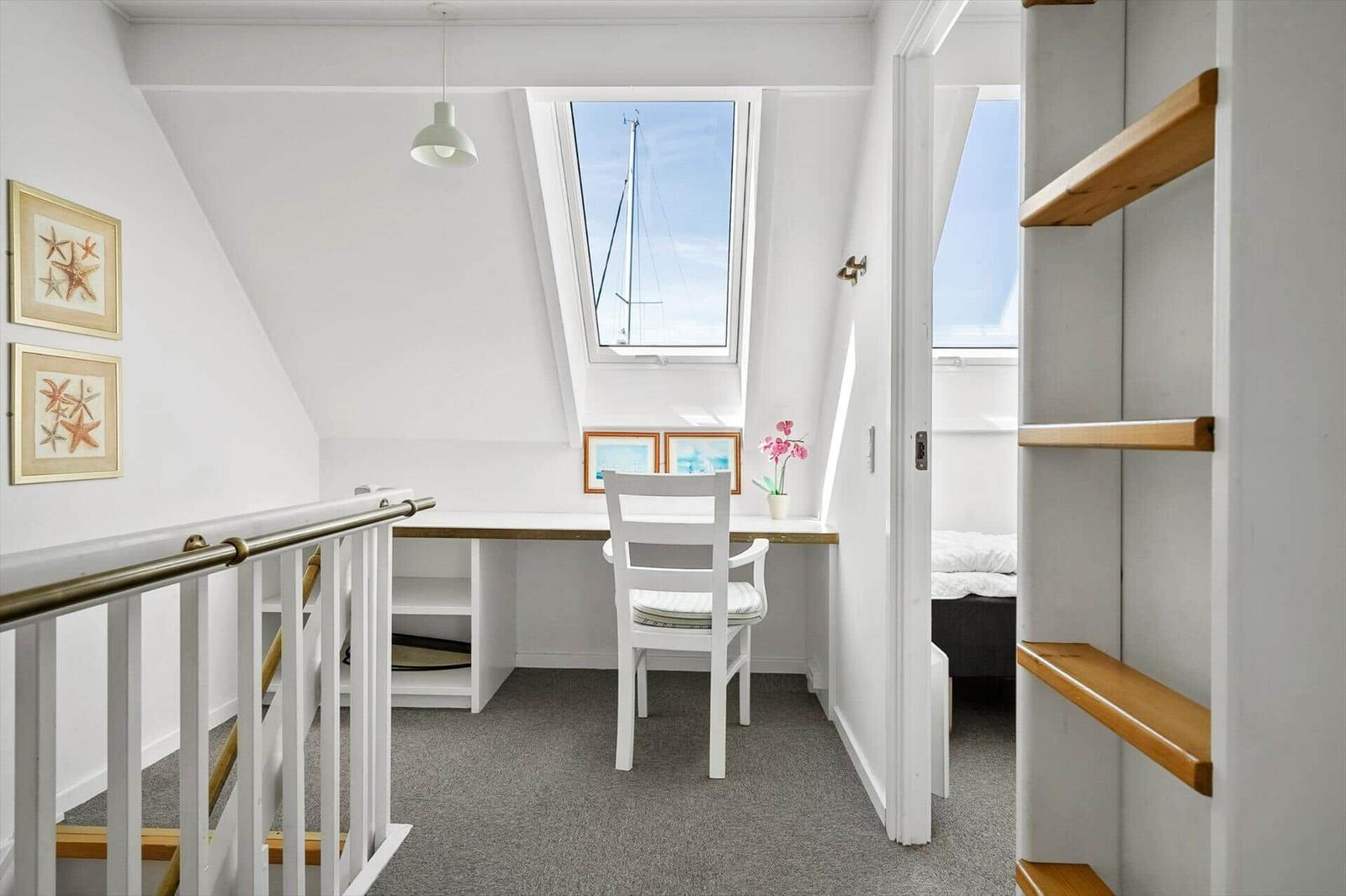 Dachgeschosszimmer mit Schreibtisch, Fenster und Bett im Hintergrund.