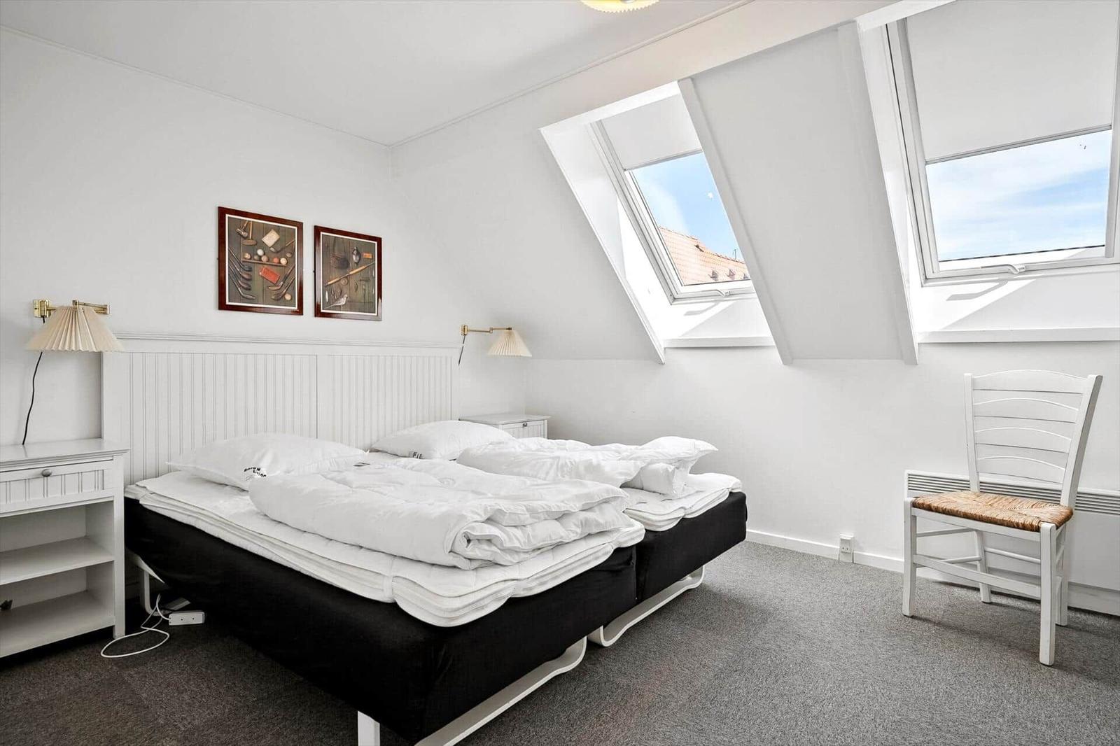 Schlafzimmer mit Dachfenstern, Bett, Stuhl und Nachttisch.