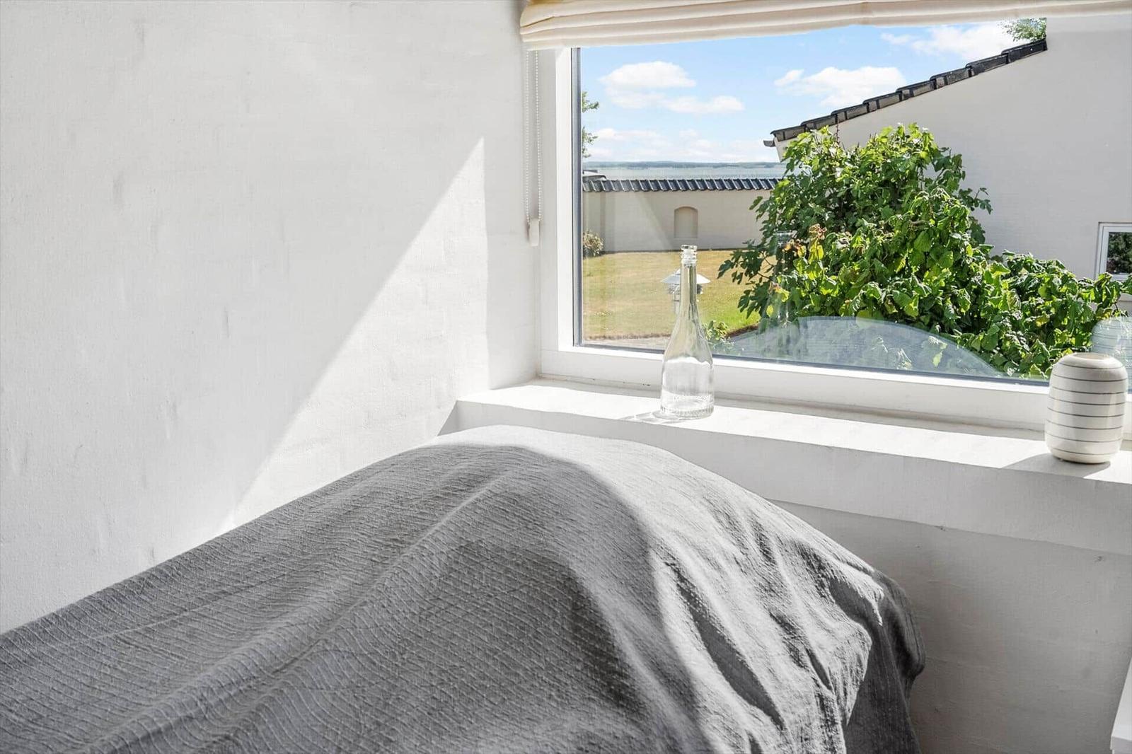 A bed with gray bedding in front of a window overlooking a garden.