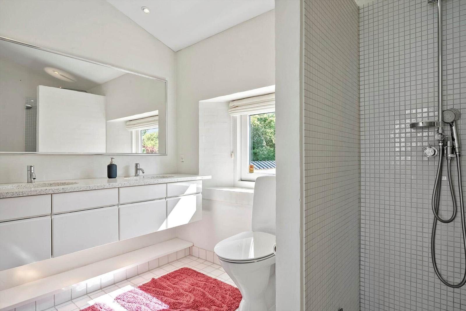 Bathroom with shower, sink, and toilet. Window with view of greenery.