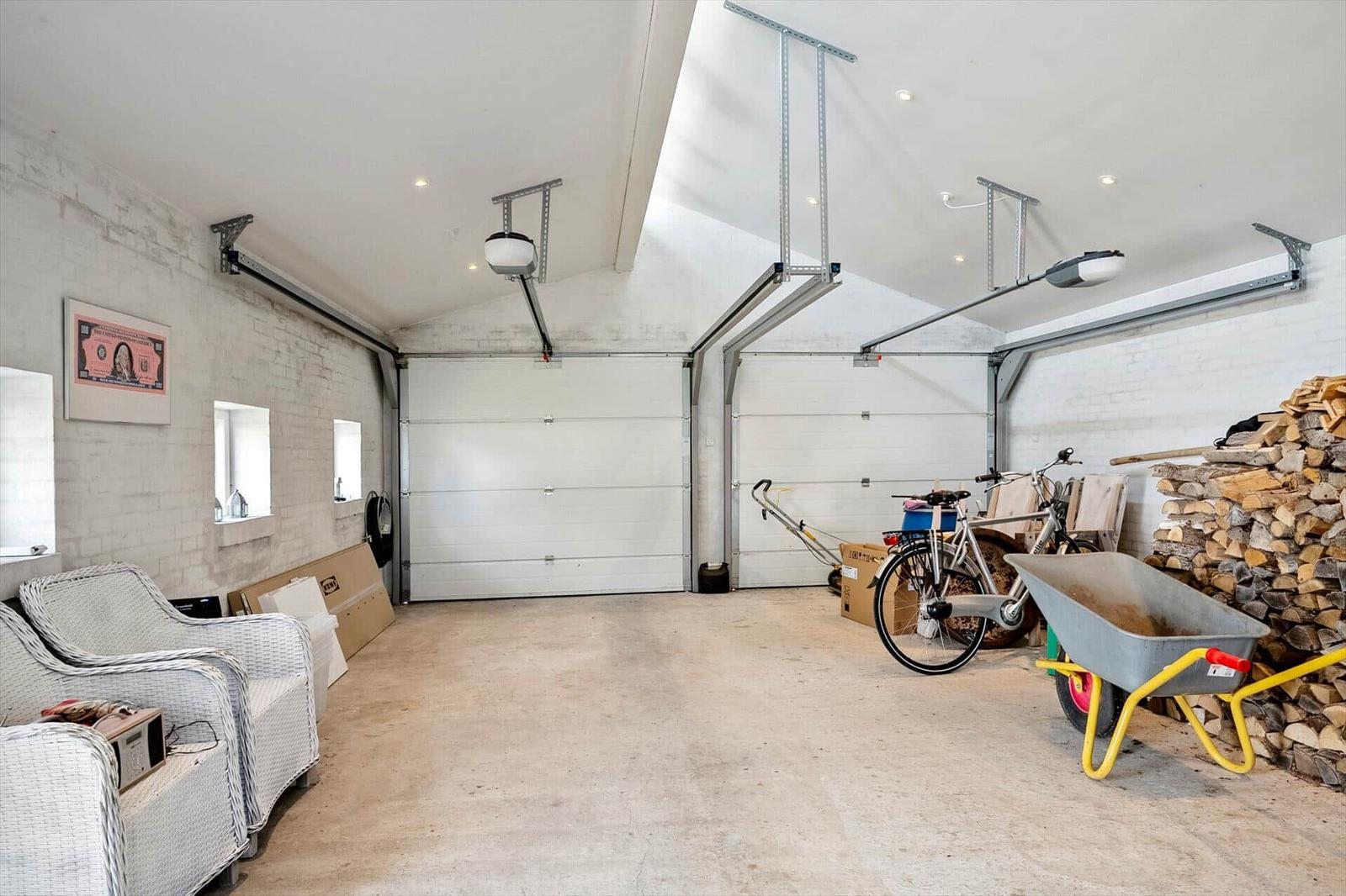 Garage with two doors, bicycle, wheelbarrow, and woodpile. Wall with windows and seating.