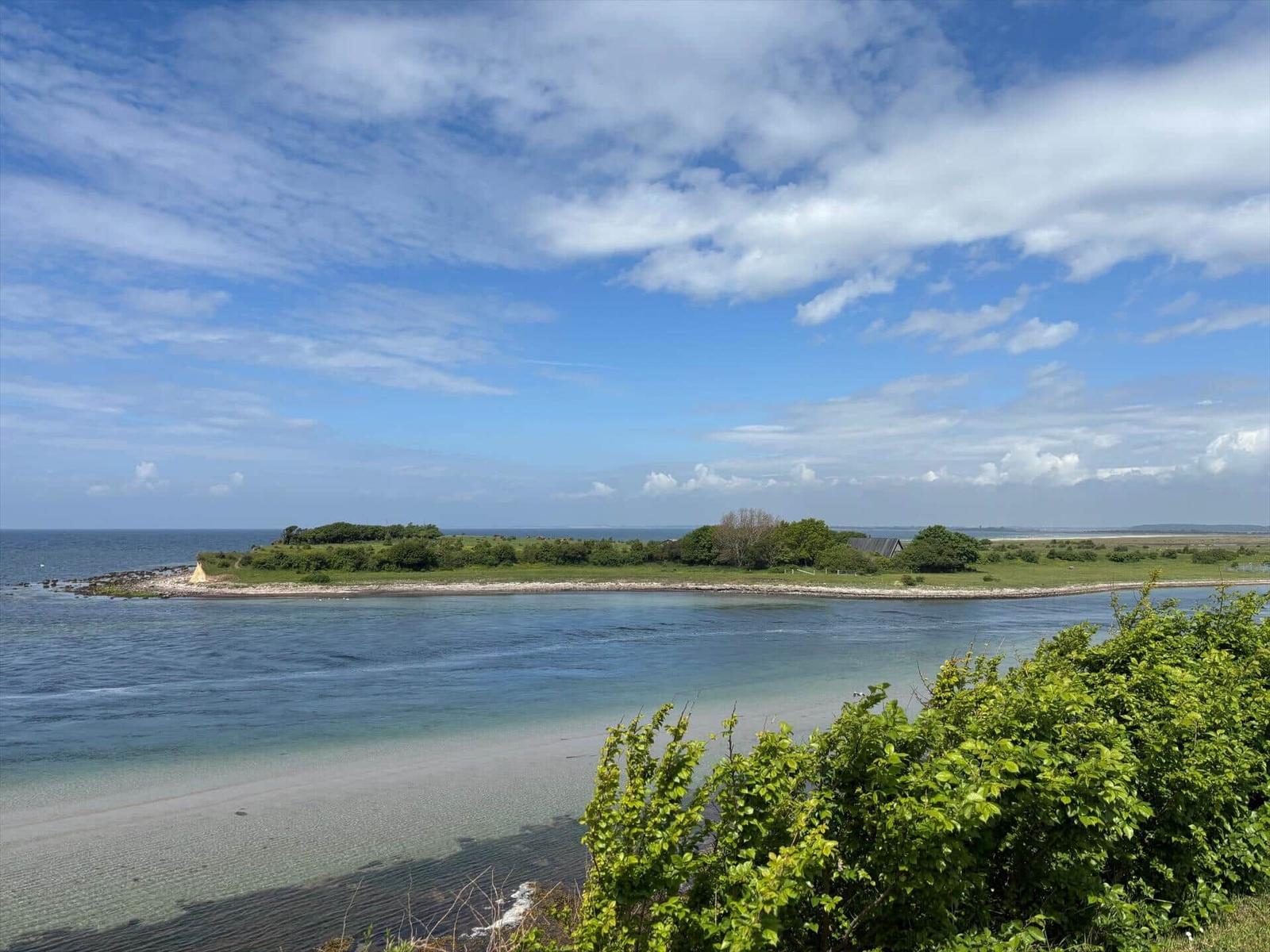 Sea with island and green landscape under blue sky with white clouds.