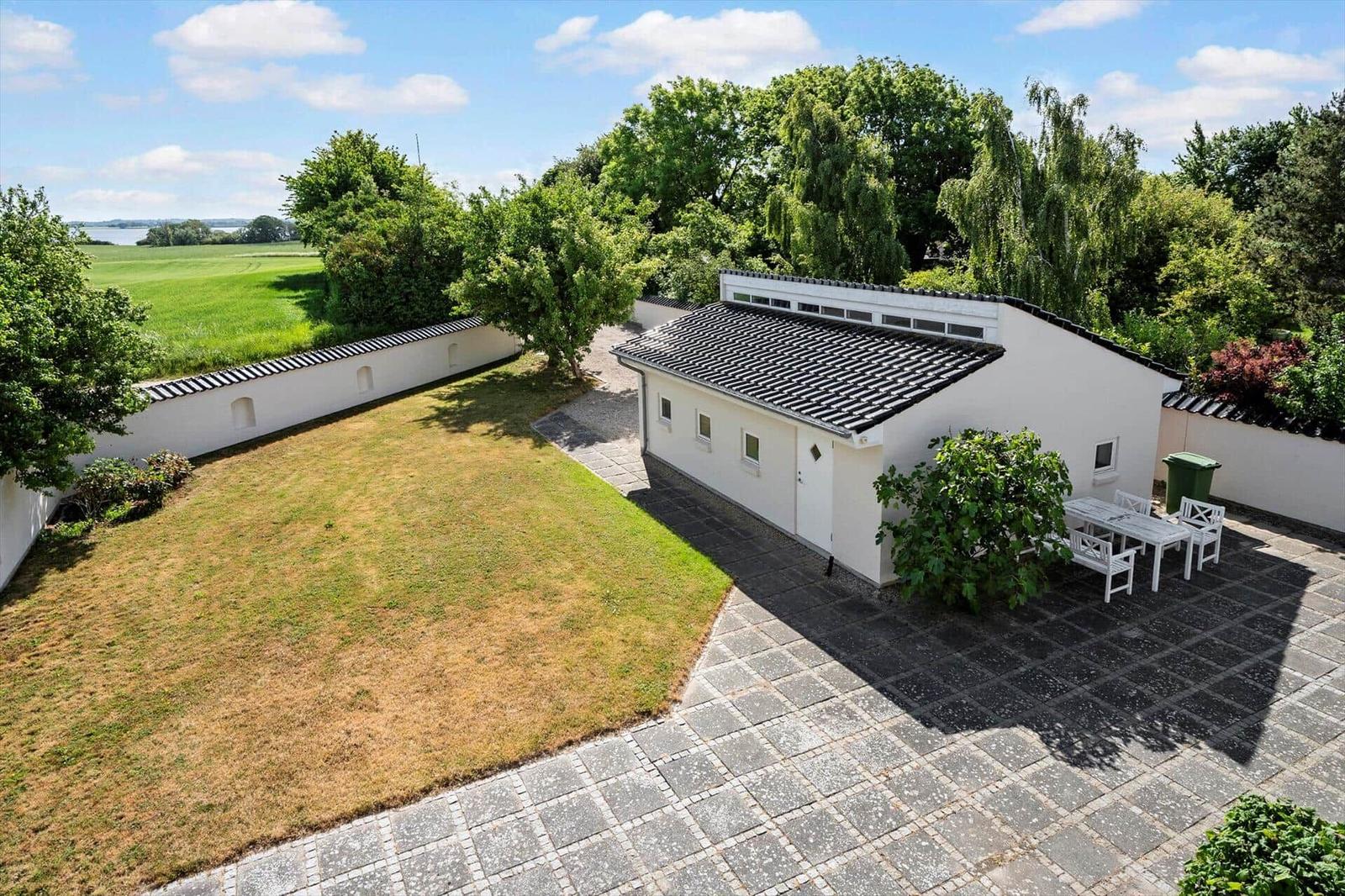 White house with terrace, garden, and view of fields and water.