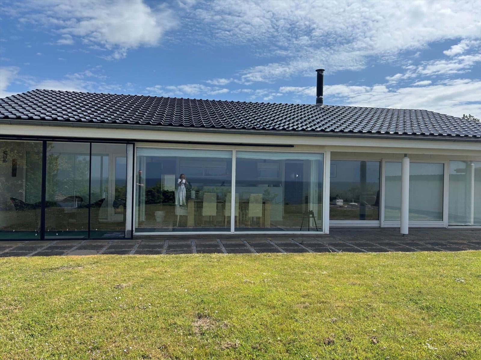 Modern villa with large glass area and terrace. View of lawn and sky.