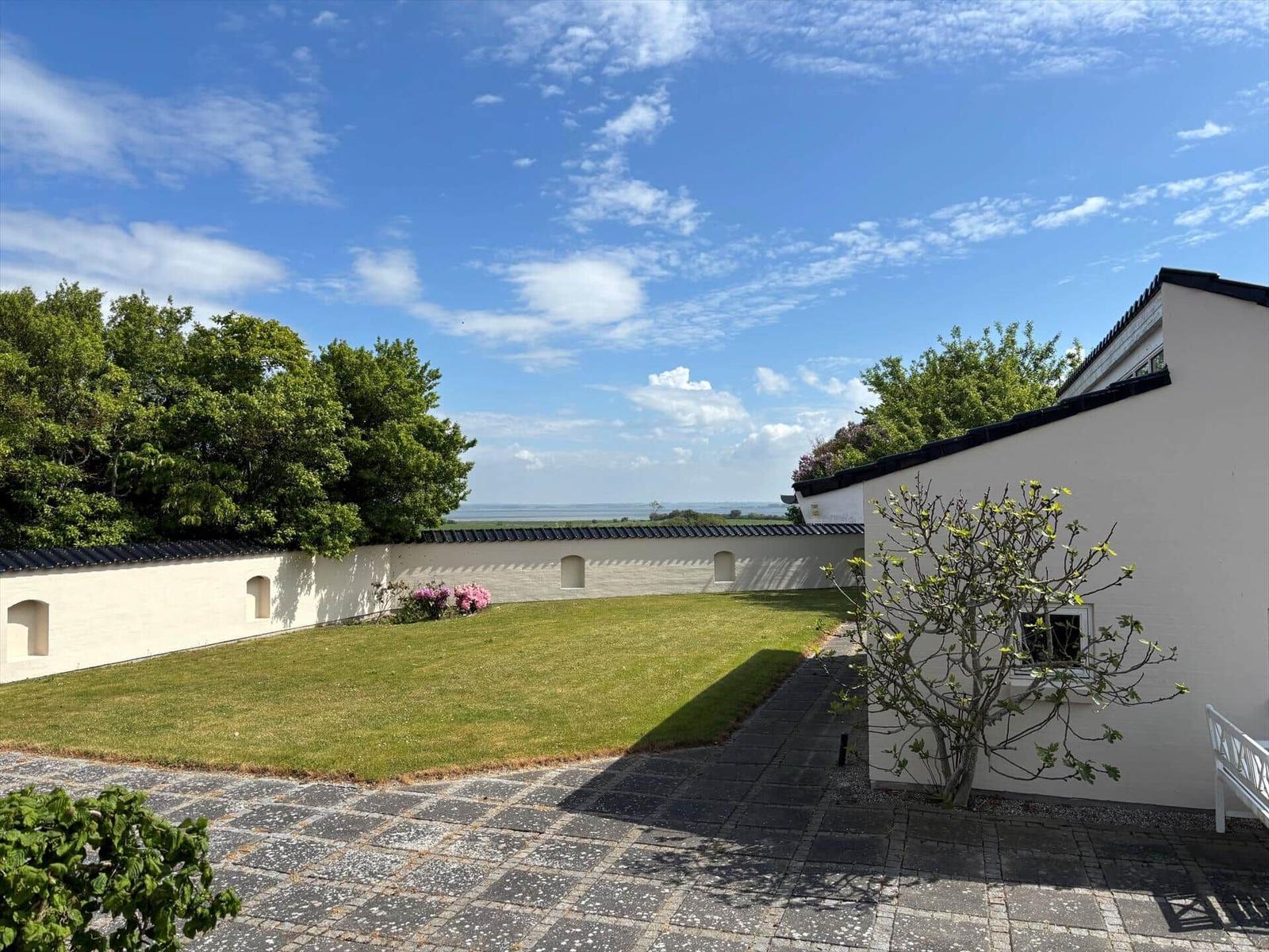 White house with garden, wall, and sea view under blue sky.