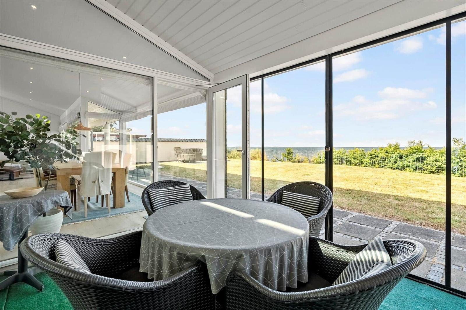 Round table with chairs under glass roof, view of lawn and horizon.