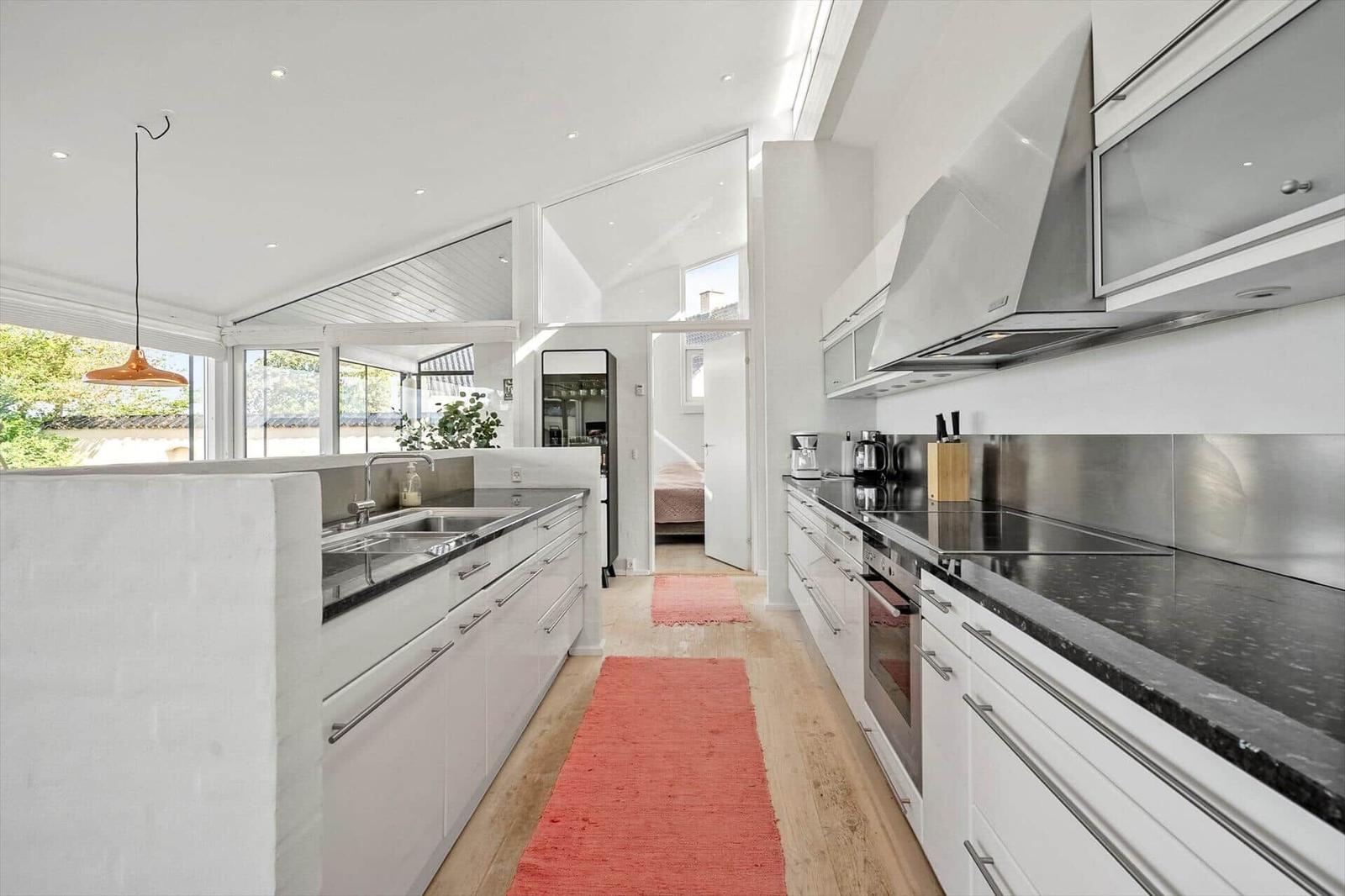 Kitchen with white cabinets, stainless steel backsplash, and red rug on wooden floor