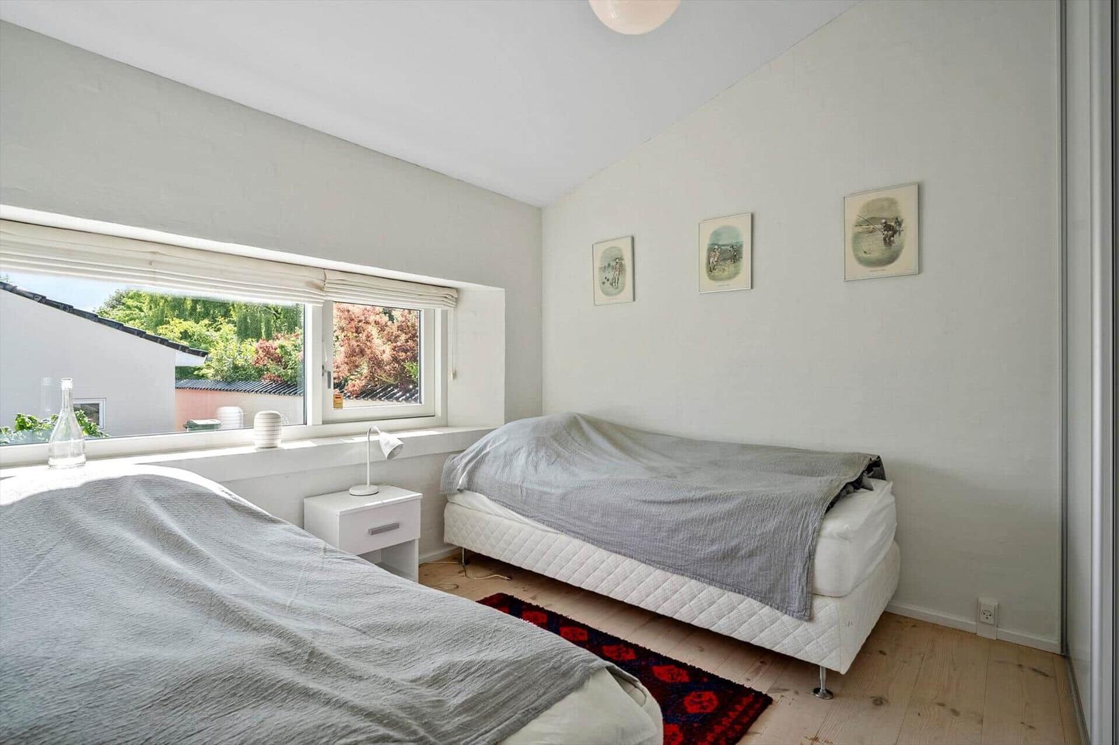 Two beds with gray blankets, window with garden view, wall with three pictures.